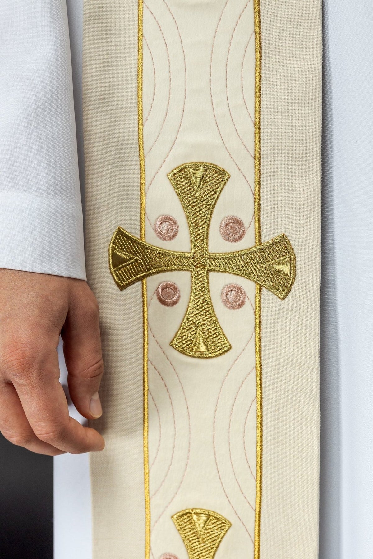 Ecru stole close-up showing a gold embroidered cross with pink circular accents