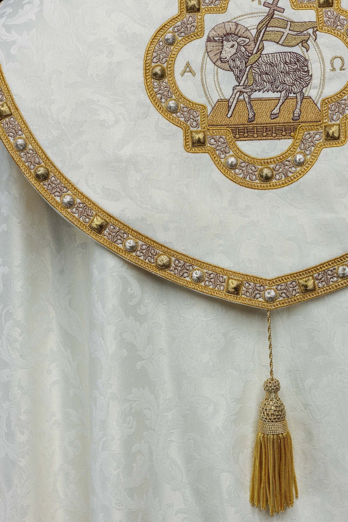 Ecru cope detail showing Paschal Lamb embroidery, jacquard fabric and ornate gold border