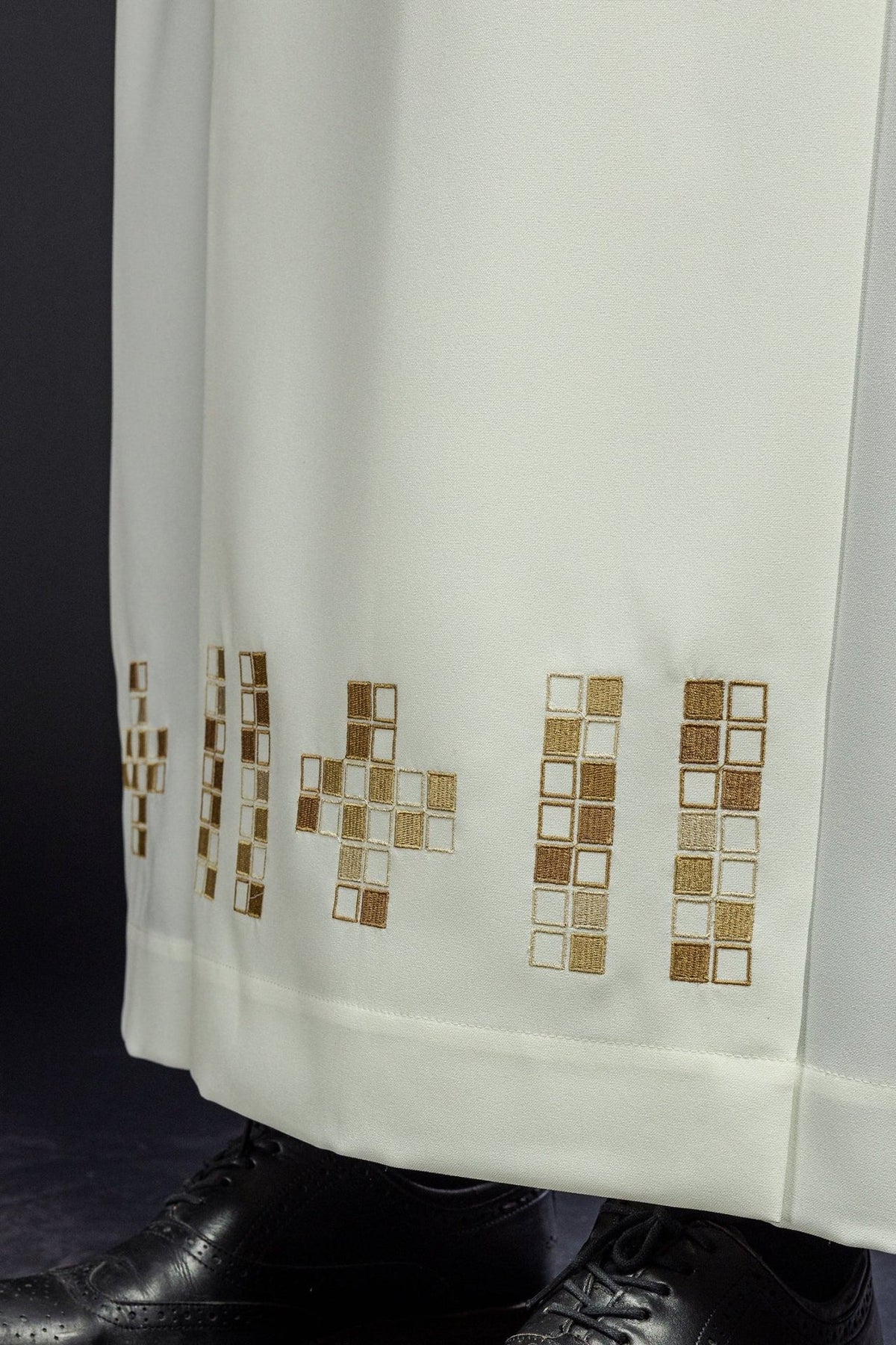 Ecru alb close-up showing gold embroidered mosaic crosses along the hem