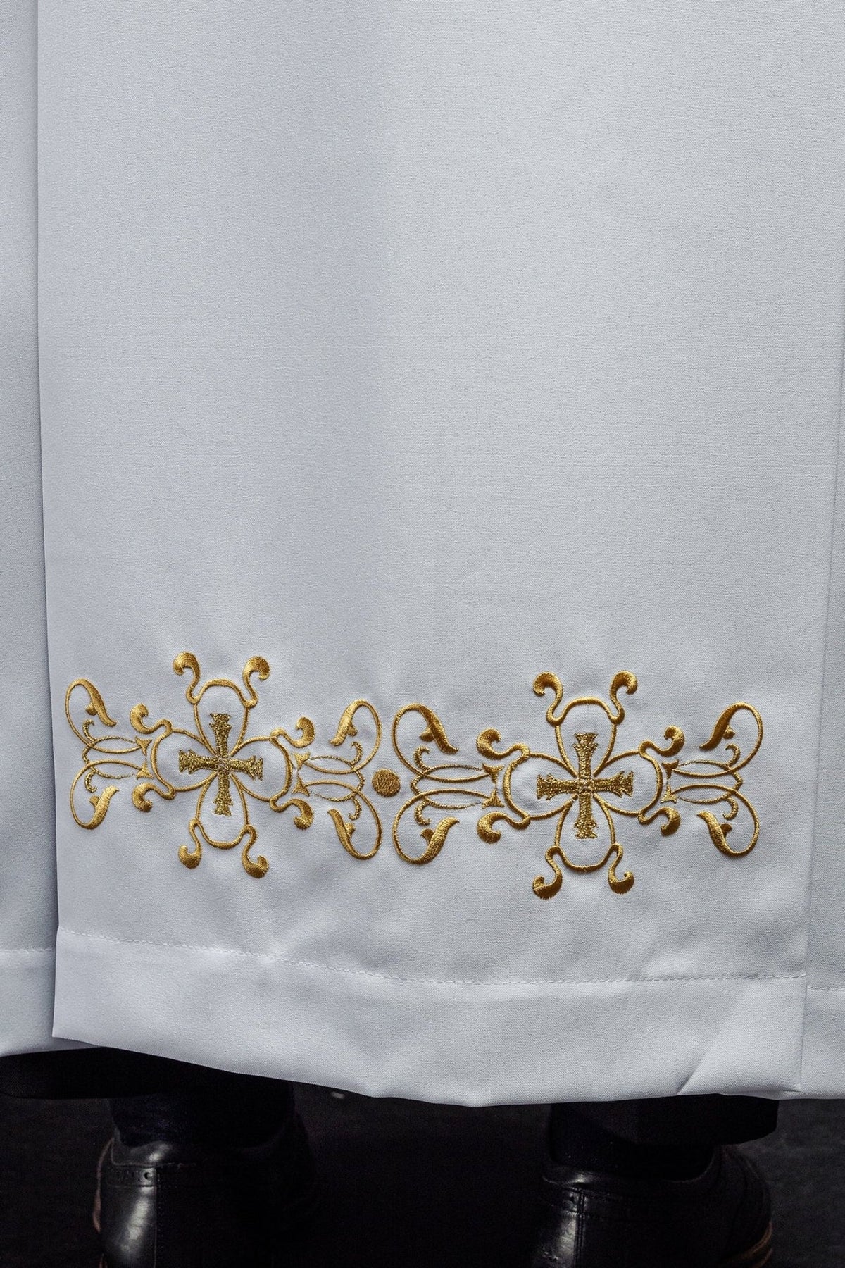 White priest alb close-up showing gold embroidered hem motif