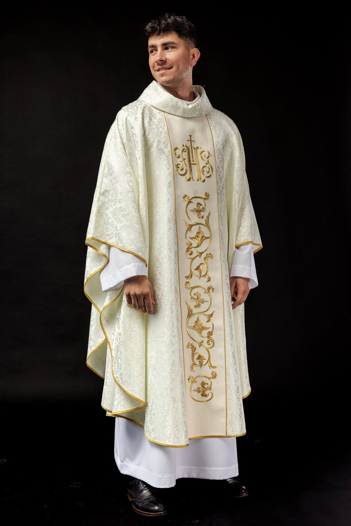 Ecru liturgical chasuble worn from the front, with gold IHS orphrey and trim