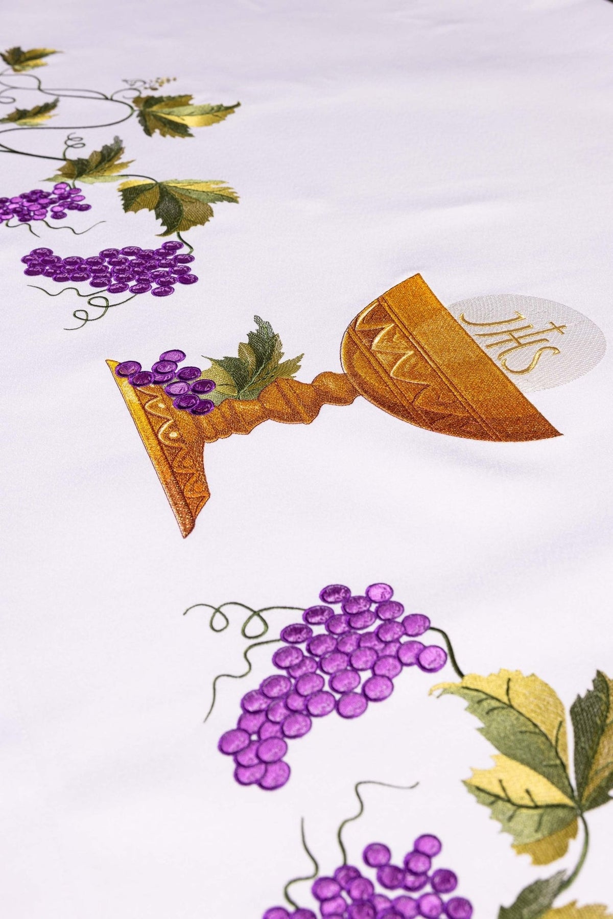 Altar cloth close-up showing gold chalice embroidery, IHS monogram, and purple grapes