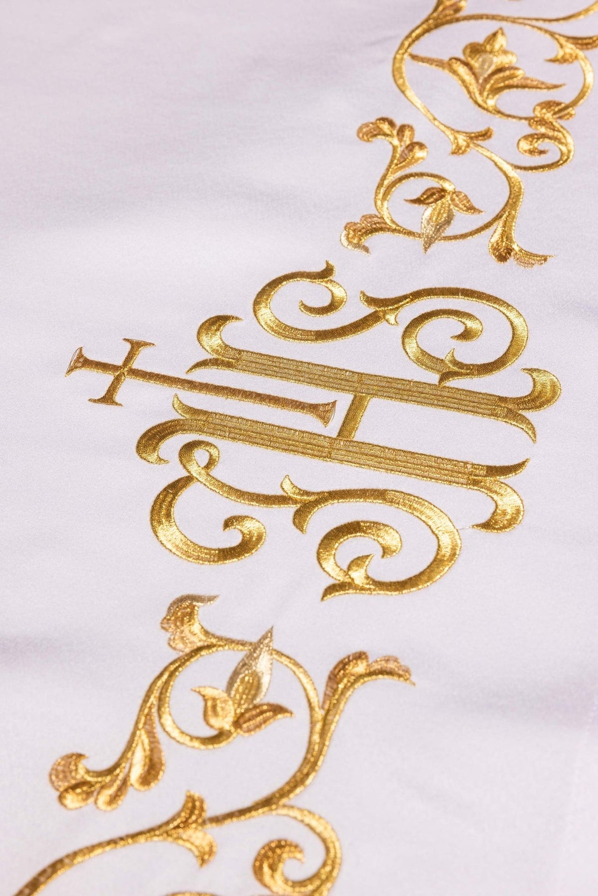 Altar cloth close-up showing gold embroidered IHS monogram and floral scrollwork on white fabric