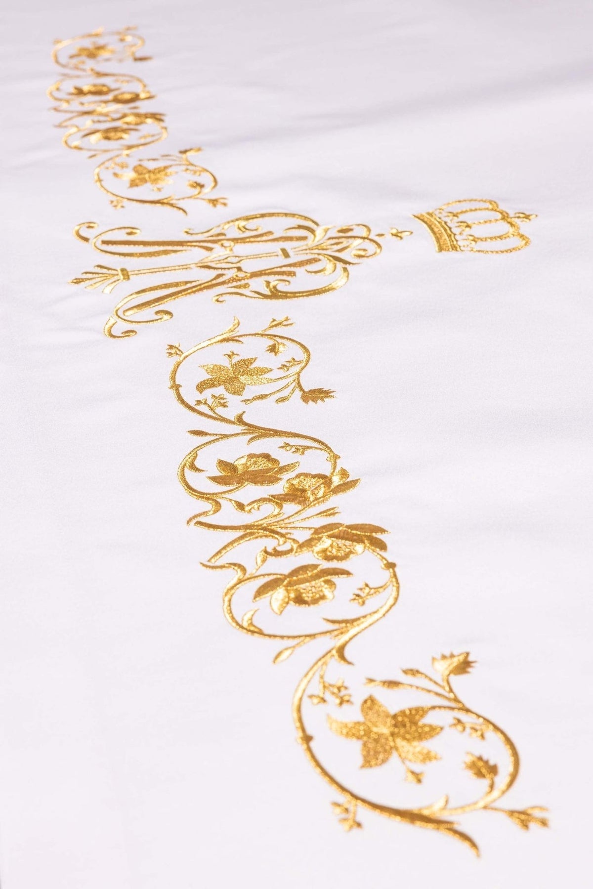White altar cloth close-up showing the gold Marian symbol and floral embroidery