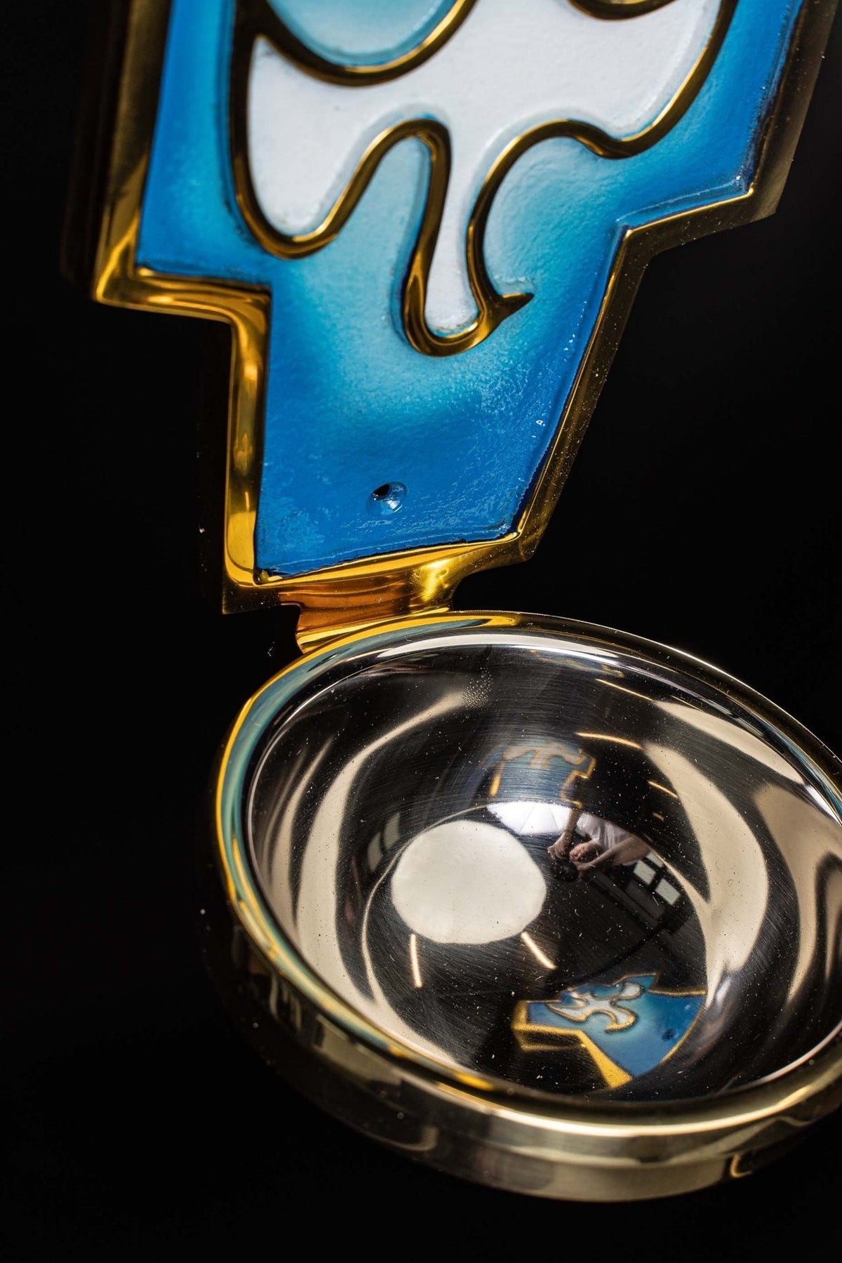Holy water font close-up showing the reflective metal basin and blue panel