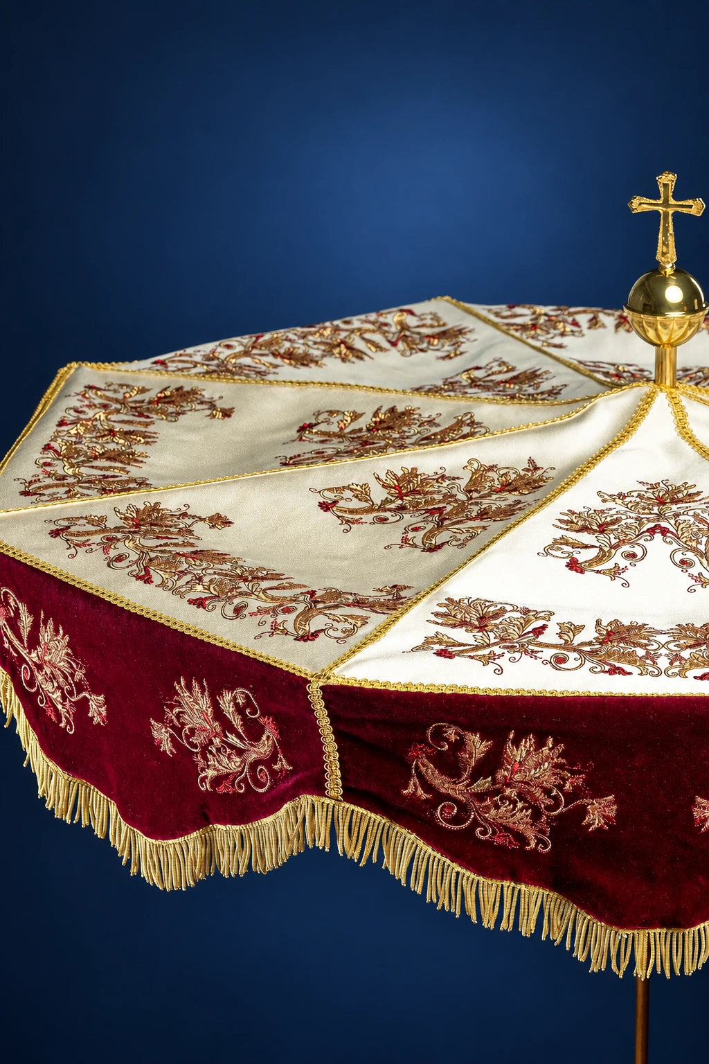 Three-quarter view of burgundy and ecru processional umbrella with embroidered floral panels and gold fringe