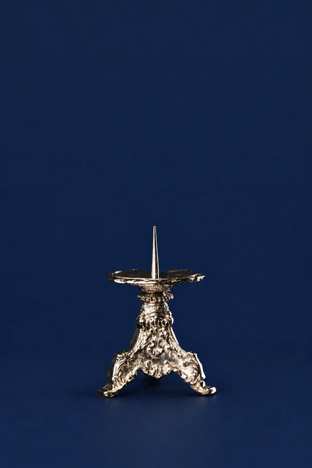 Three-quarter view of a small nickel-plated brass candlestick with ornate tripod base and central spike
