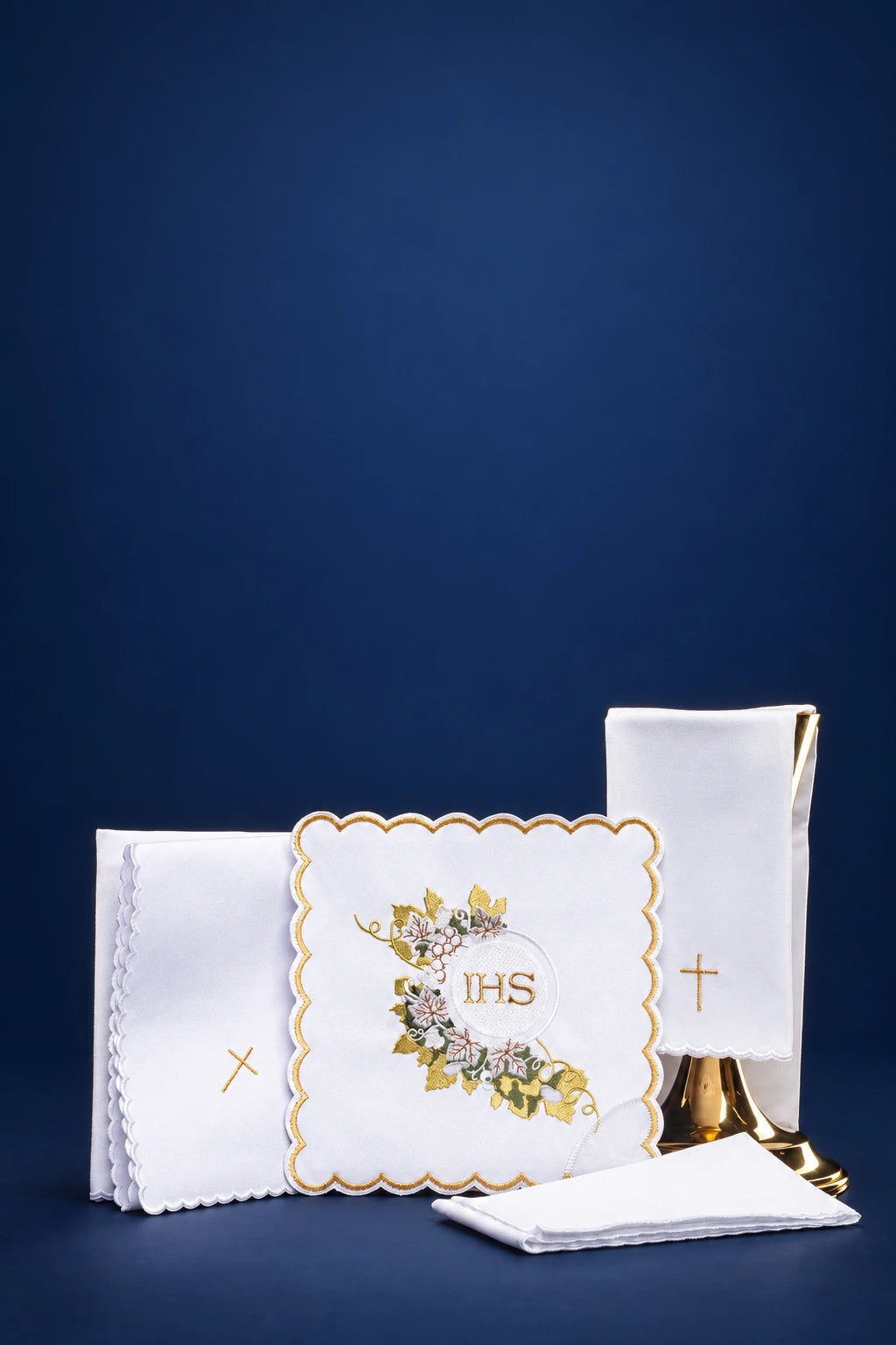 White altar linen set with embroidered IHS square, small cross cloths, and folded purificator on a chalice