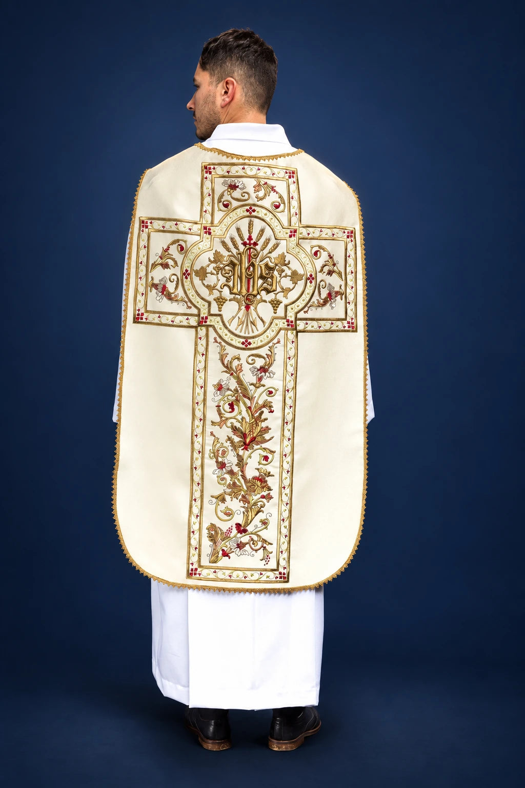 Back view of a cream Roman chasuble with ornate embroidered cross and IHS medallion center motif