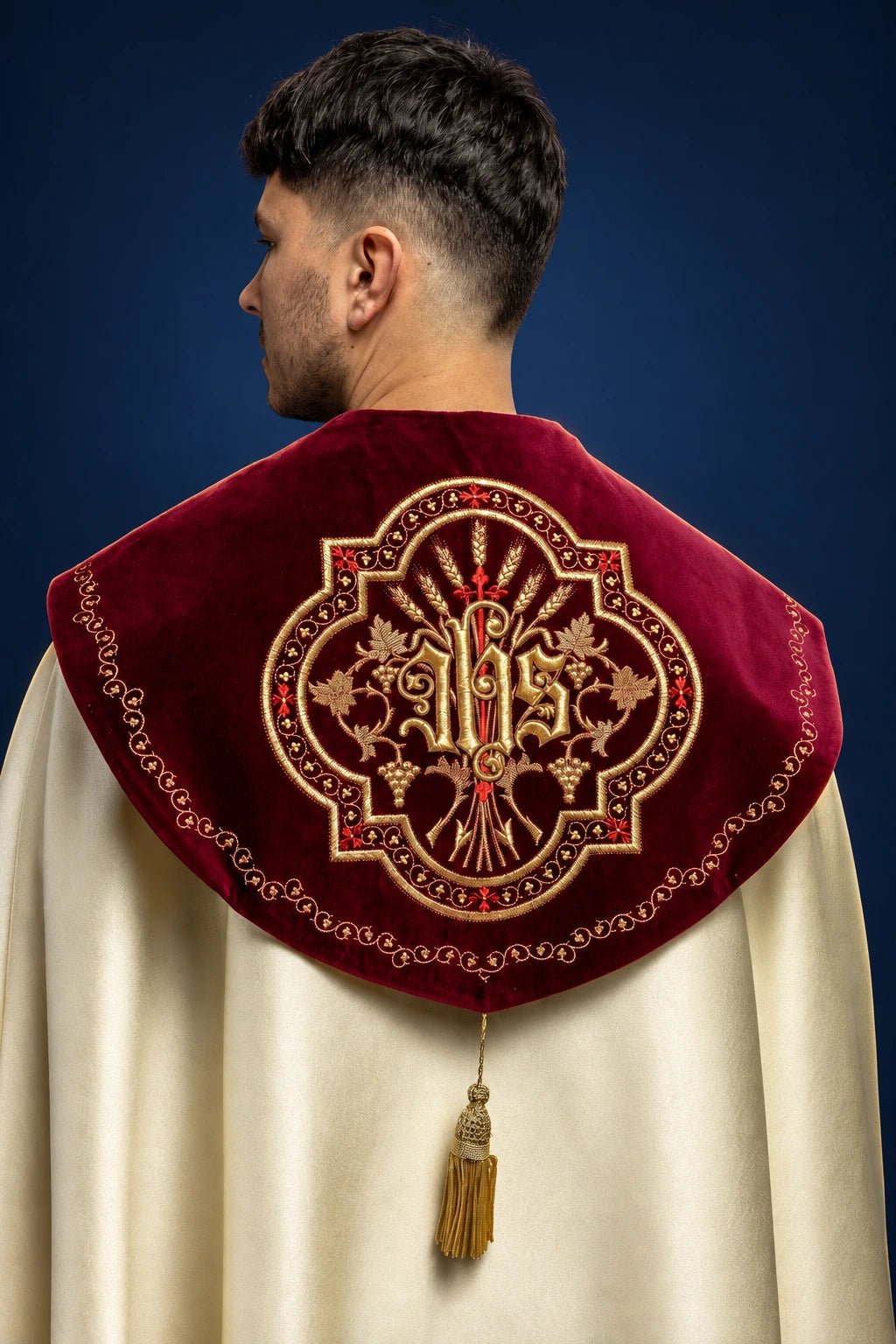 Back view of ecru cope with burgundy velvet yoke, IHS and floral embroidery, and gold tassel clasp
