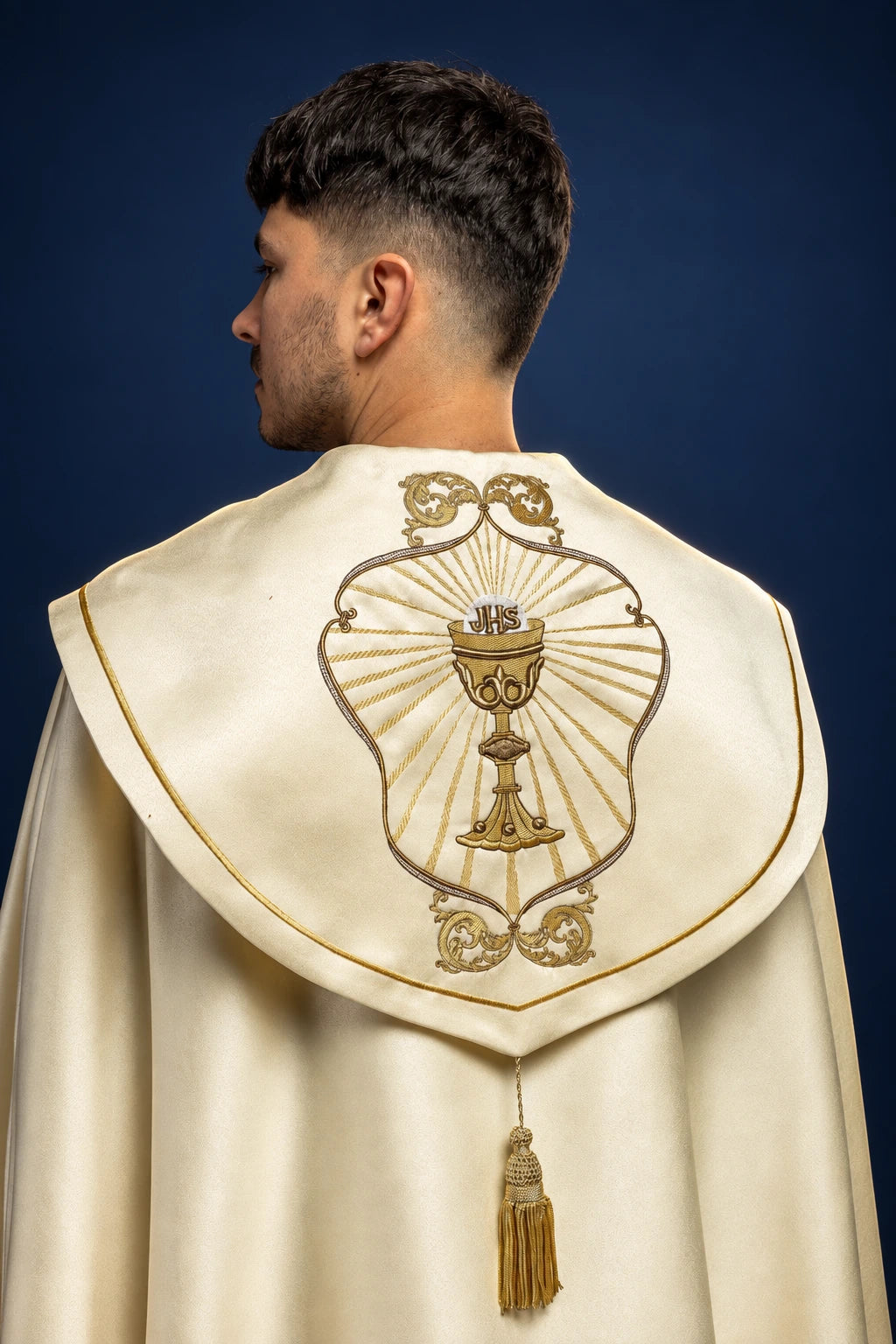 Back view of an ecru liturgical cope with chalice and IHS embroidery on the hood and a tassel clasp