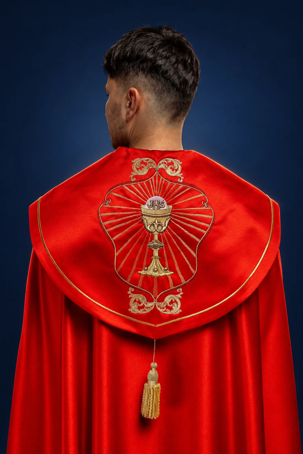 Back view of a red cope with embroidered chalice and IHS medallion on the hood and gold tassel closure