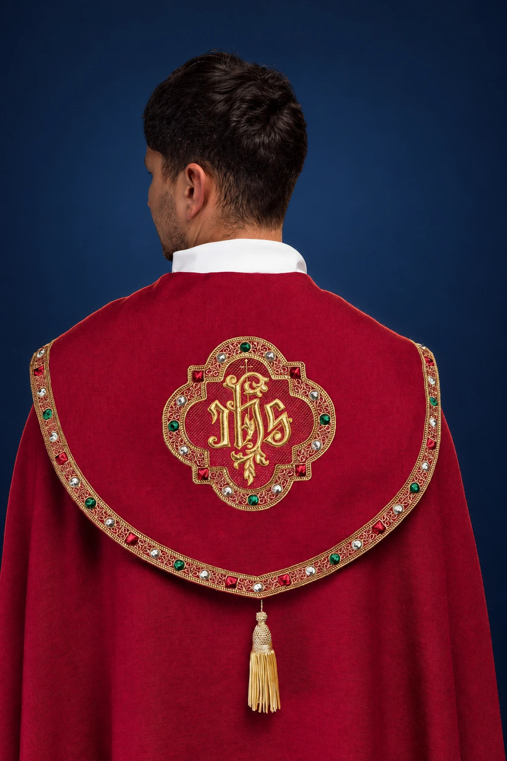 Back view of a red cope with gold IHS embroidery and jeweled trim, ending in a tassel clasp