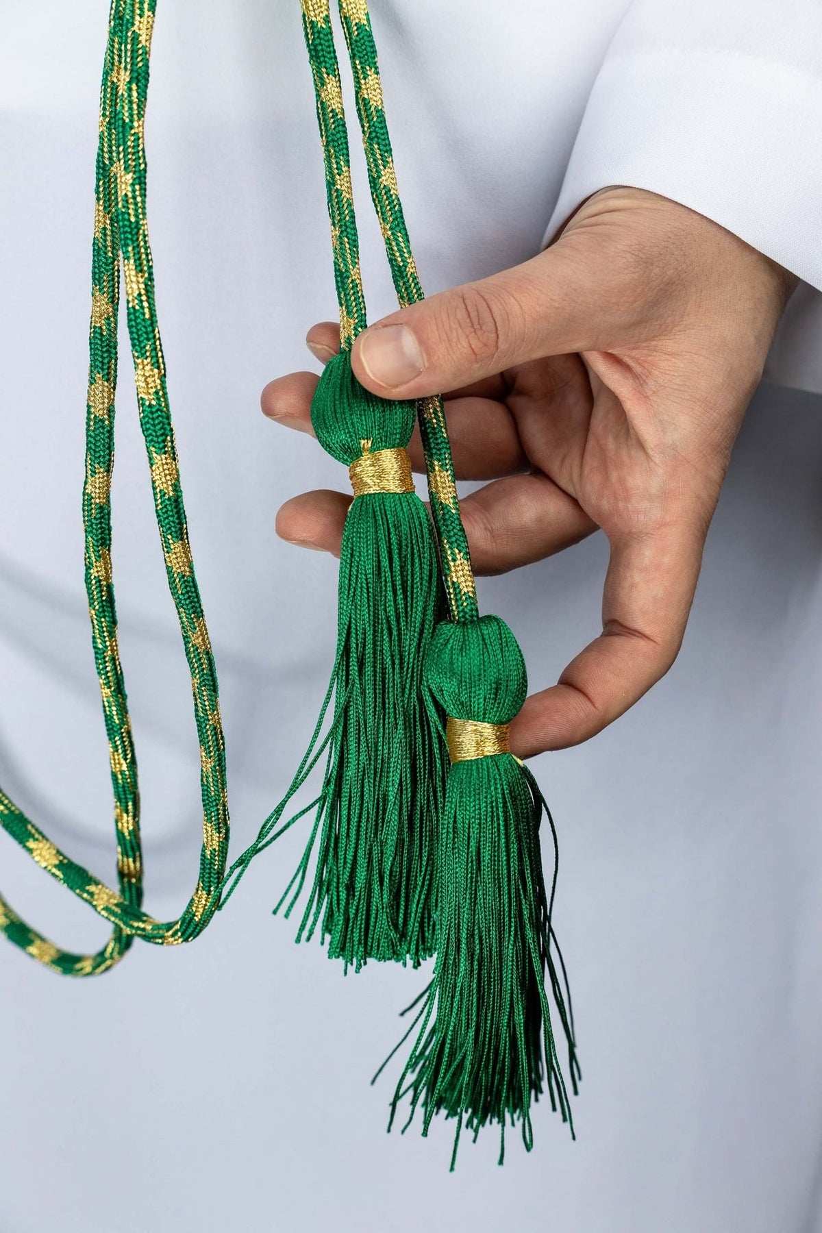 Green and gold cincture close-up showing two green tassels with gold bands