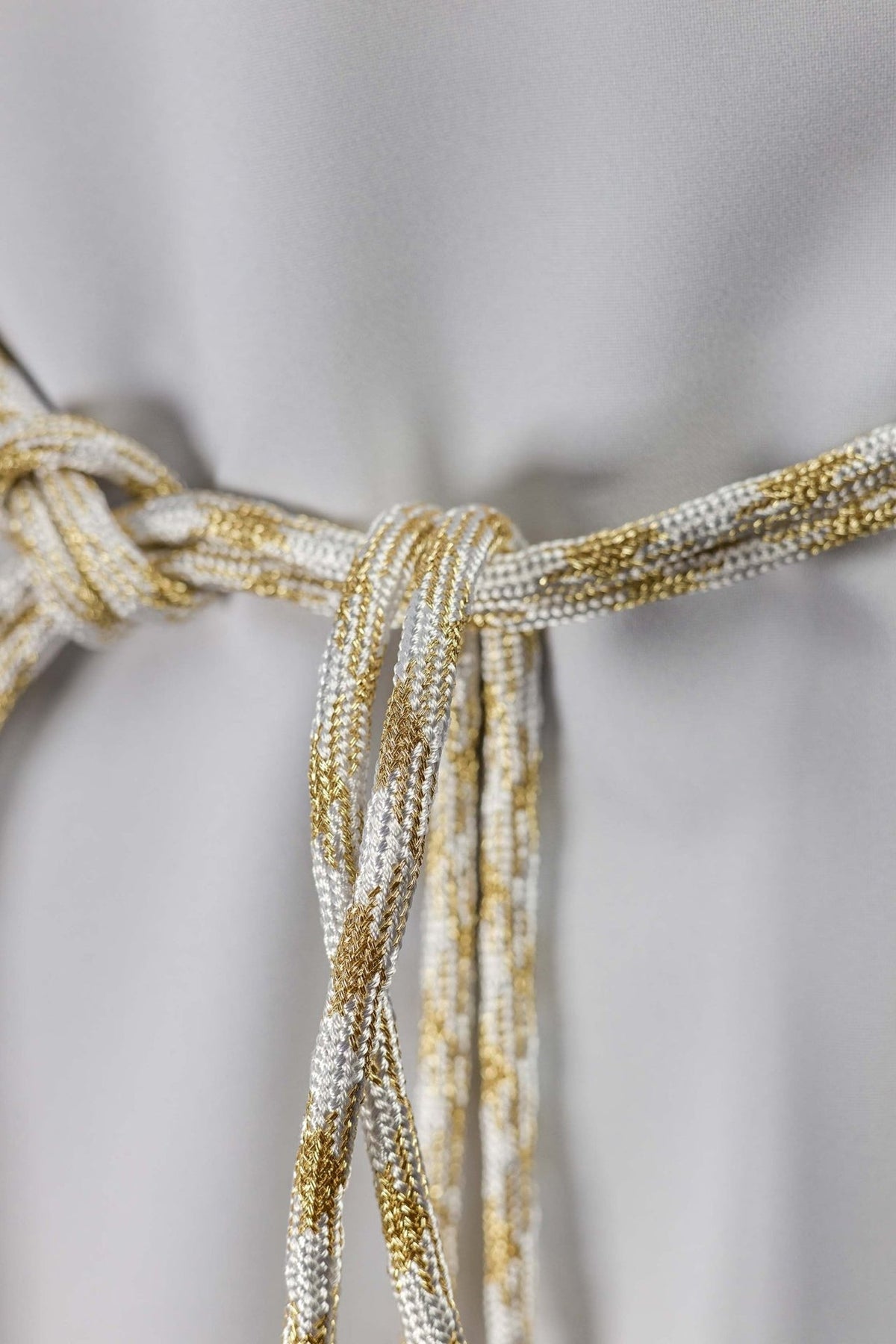 White and gold cincture close-up showing braided cord and central knot