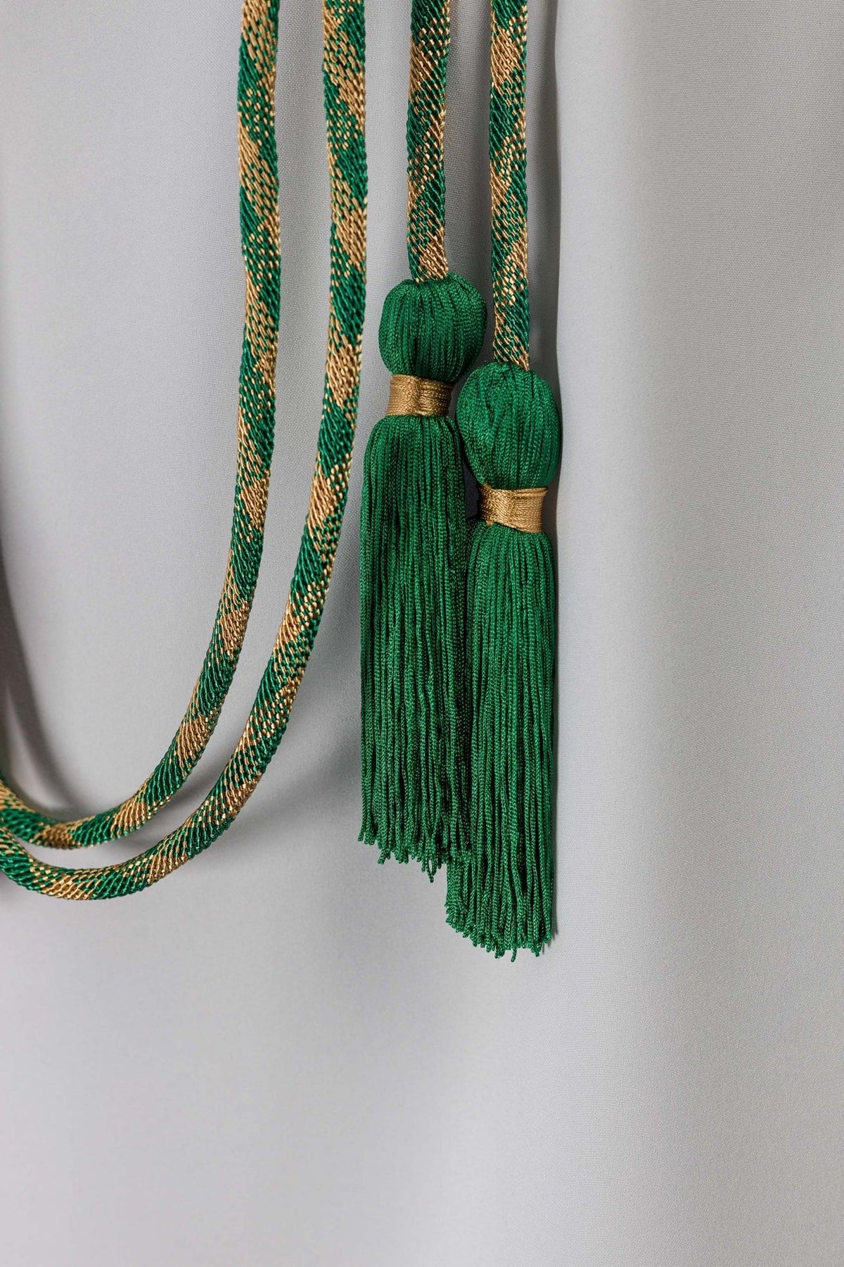 Green and gold cincture close-up showing two green tassels with gold bands