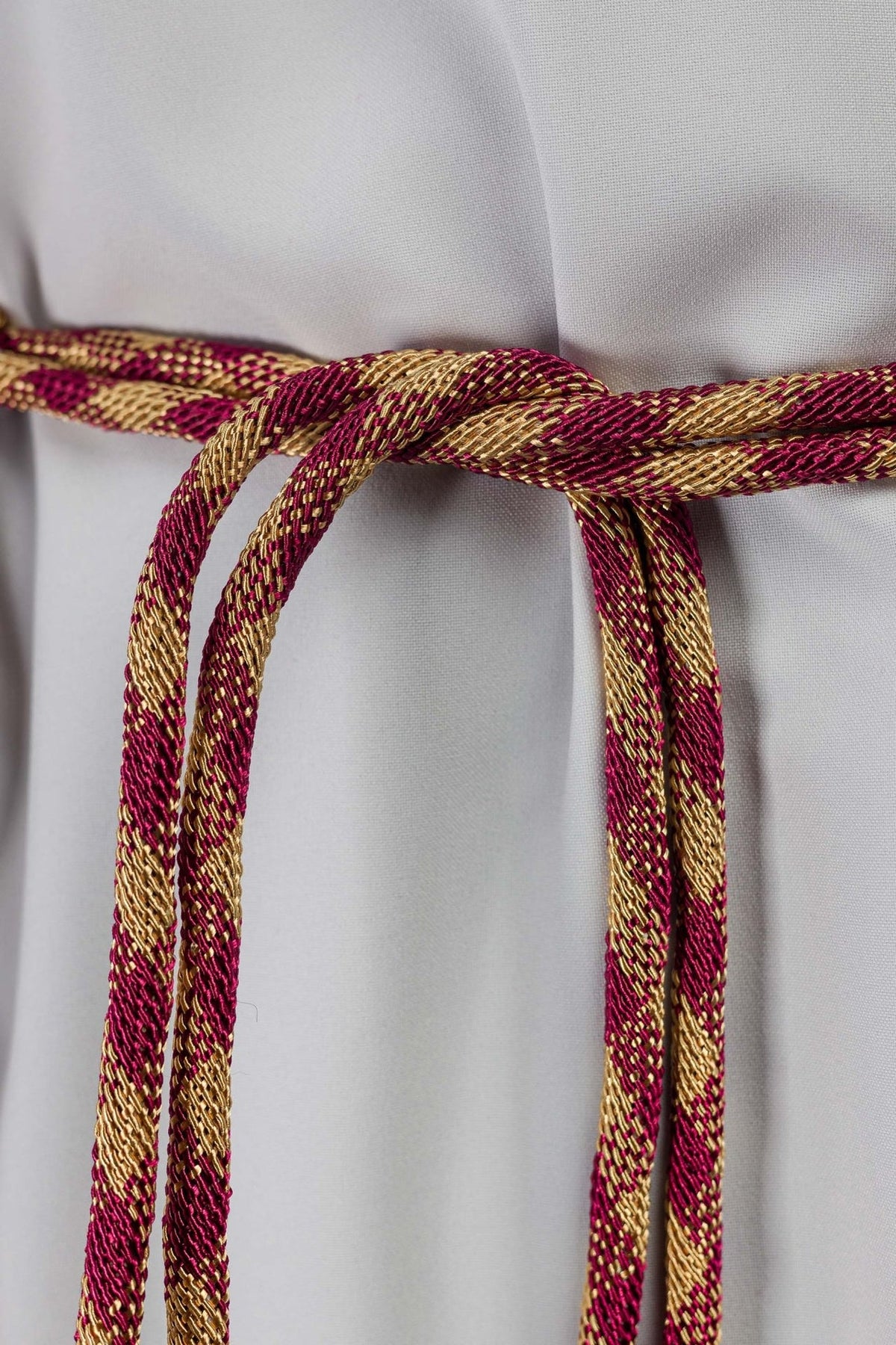Red-and-gold cincture close-up showing twisted woven cords