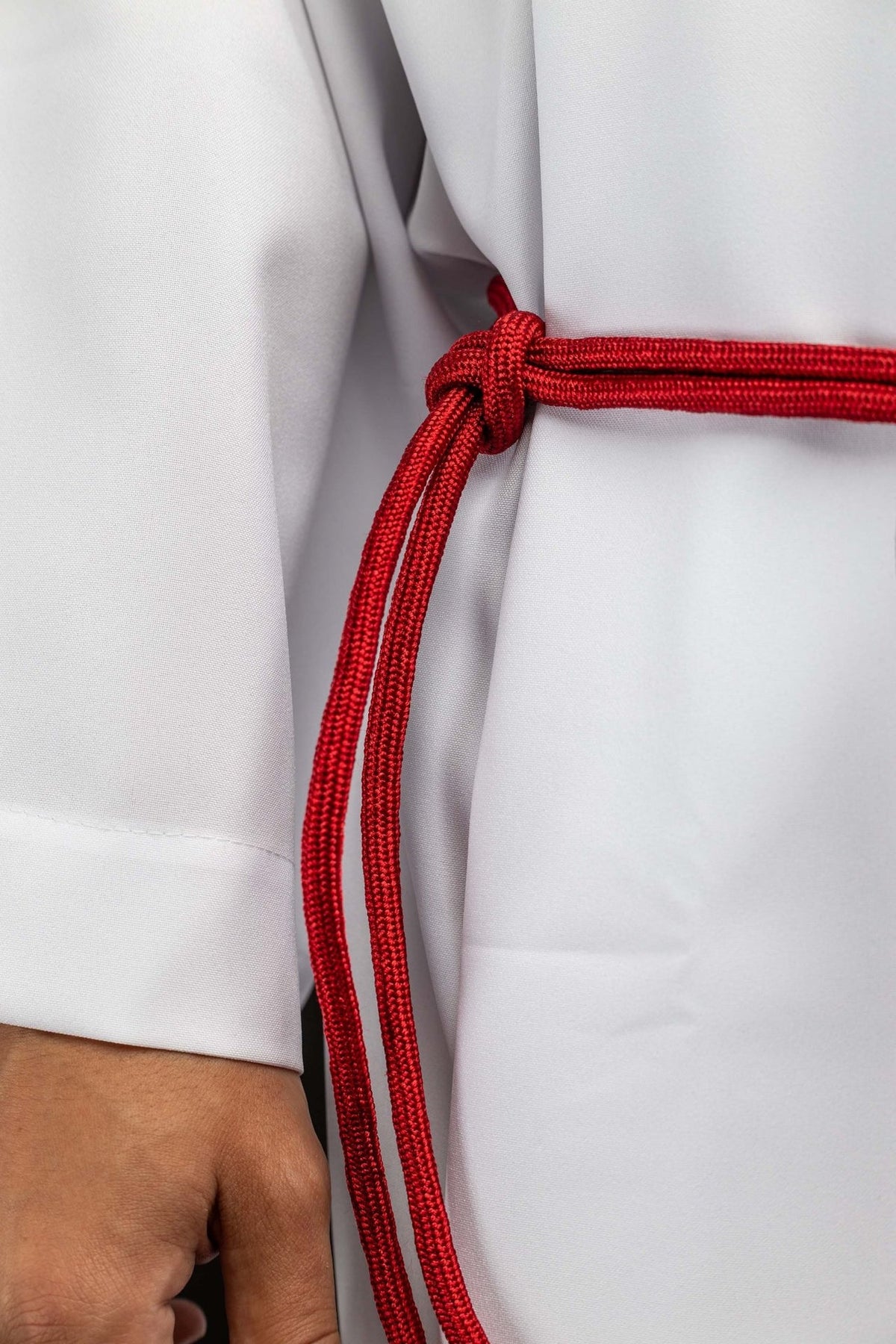 Red liturgical cincture close-up showing the knotted red cord and looped ends