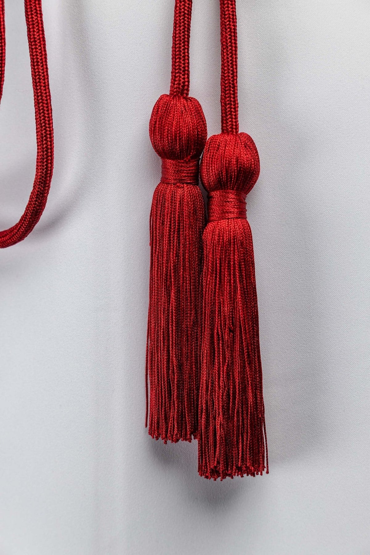 Red liturgical cincture tassels close-up showing rounded tops and long hanging fringe