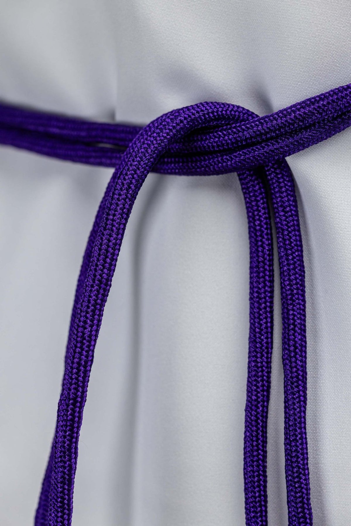 Purple cincture close-up showing the overlapping braided cord at the waist