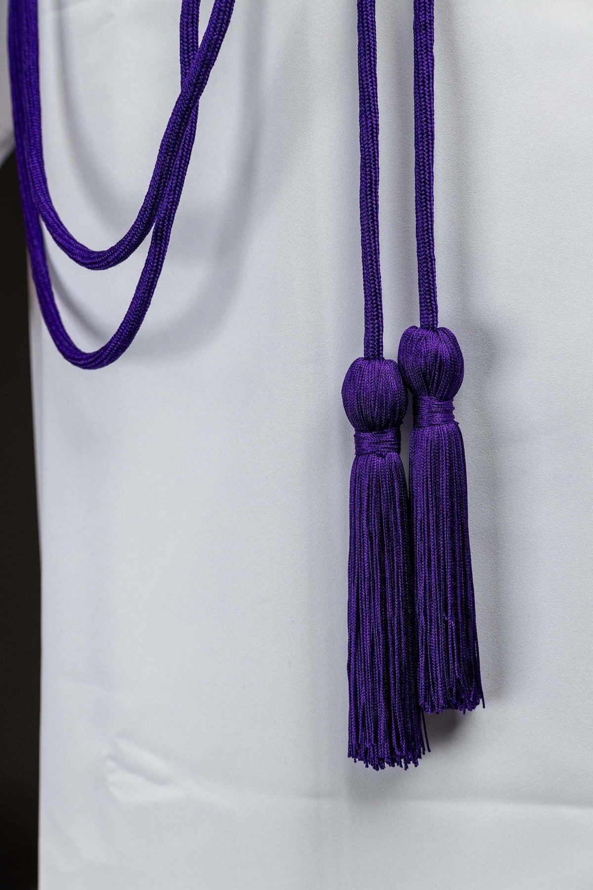 Purple cincture showing two long tassels with rounded tops and fringe