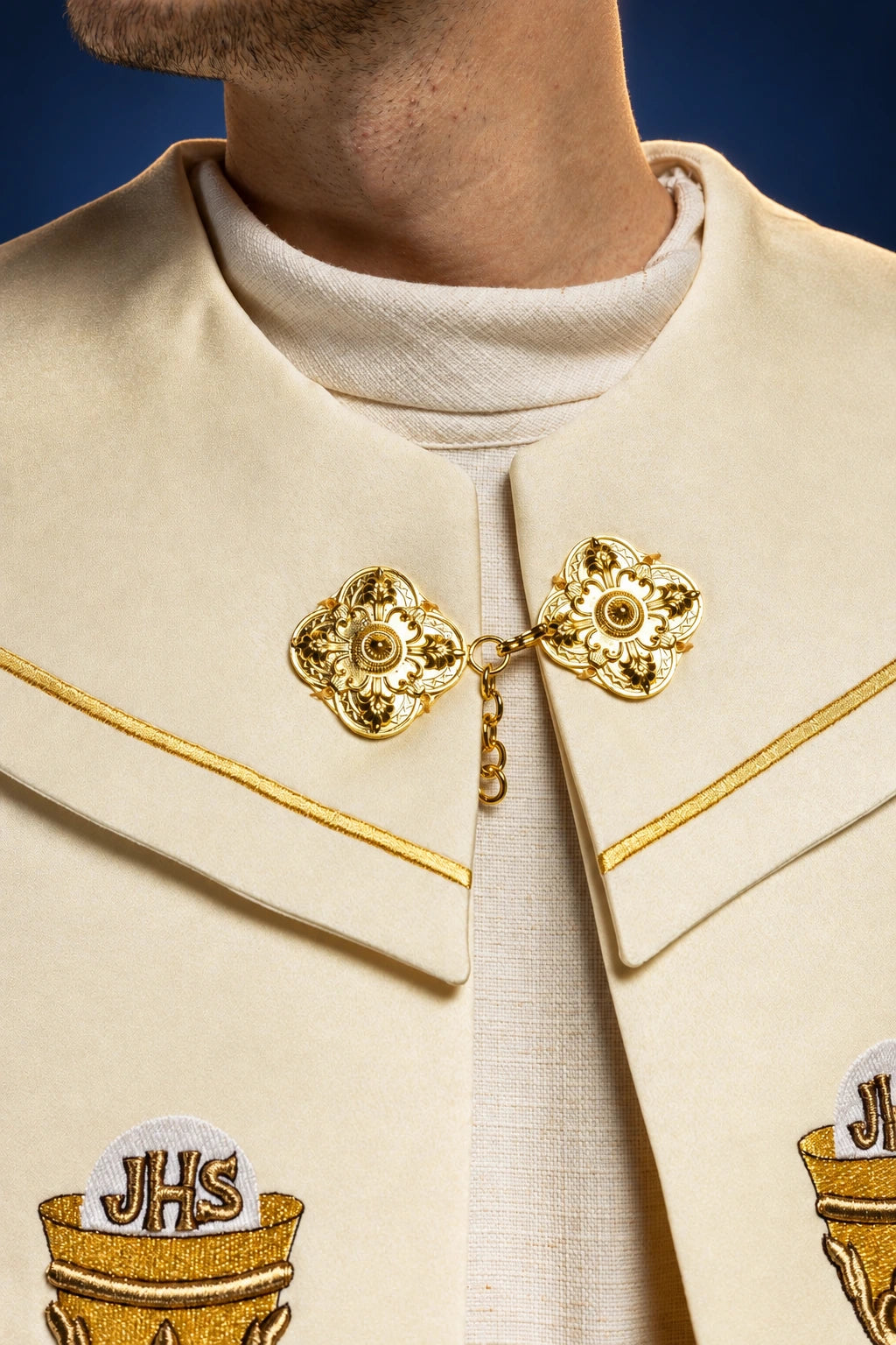 Close-up of the ecru cope front clasp with gold embroidery and partial JHS chalice motifs