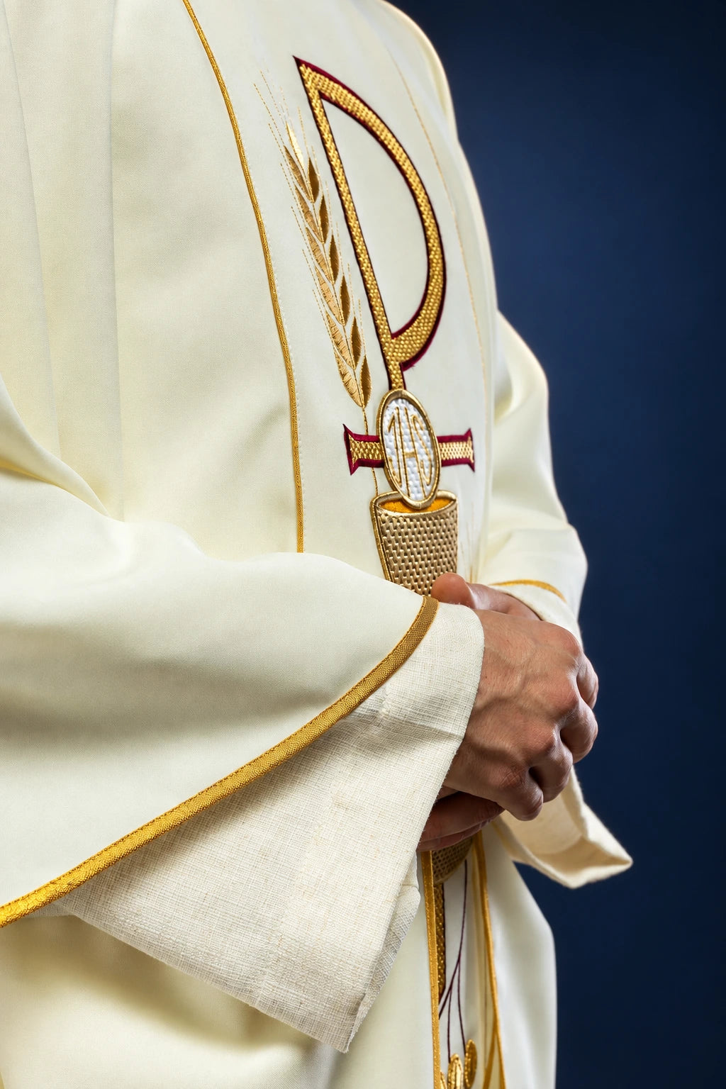 Close-up of the front chest on an ecru chasuble, showing the IHS chalice embroidery and gold-trimmed sleeve