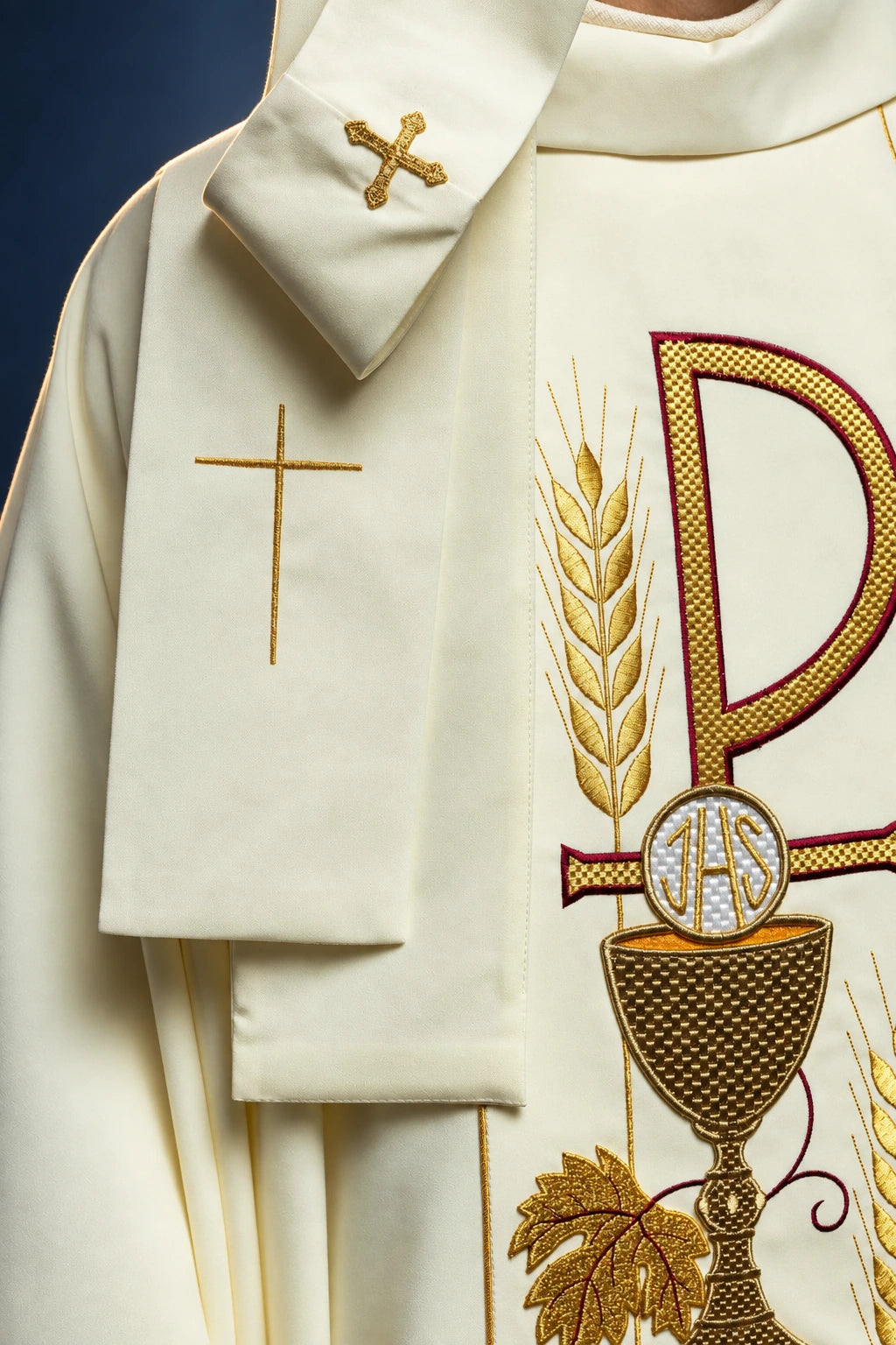 Close-up of the front left side of an ecru chasuble, showing a gold cross and shoulder embroidery beside the IHS chalice