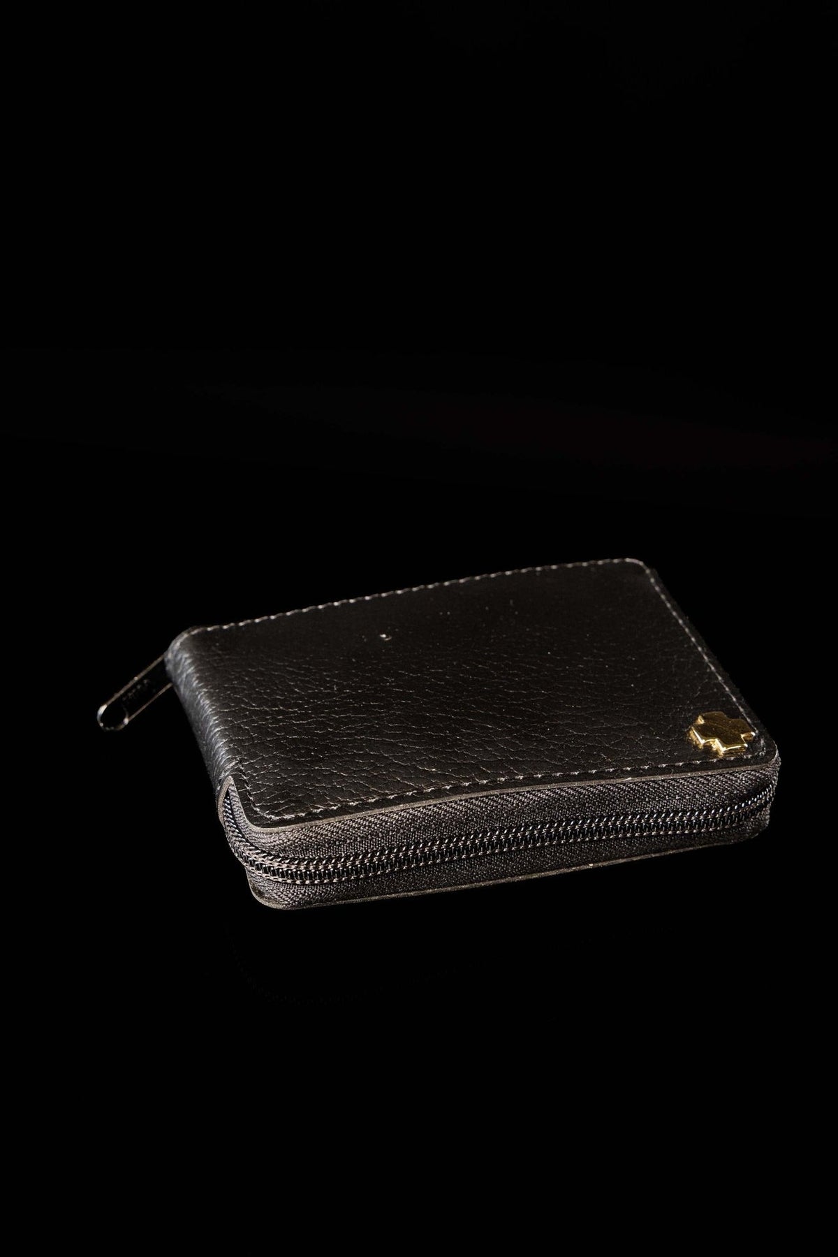 Burse with liturgical supplies closed, showing black textured exterior, zipper and gold cross emblem
