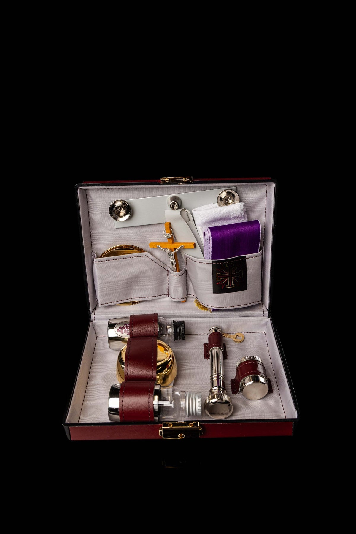 Open liturgical equipment suitcase showing organized compartments and burgundy straps