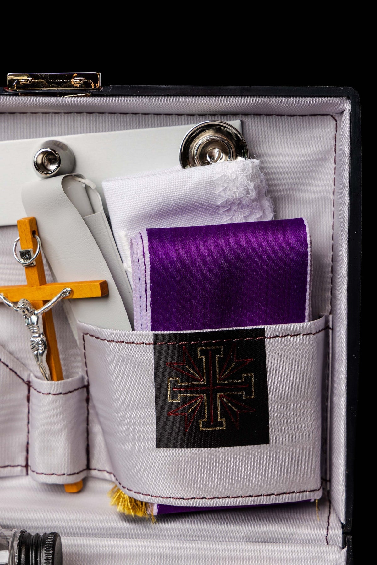 Close-up of liturgical suitcase compartment with purple cloth and gold-and-red cross emblem