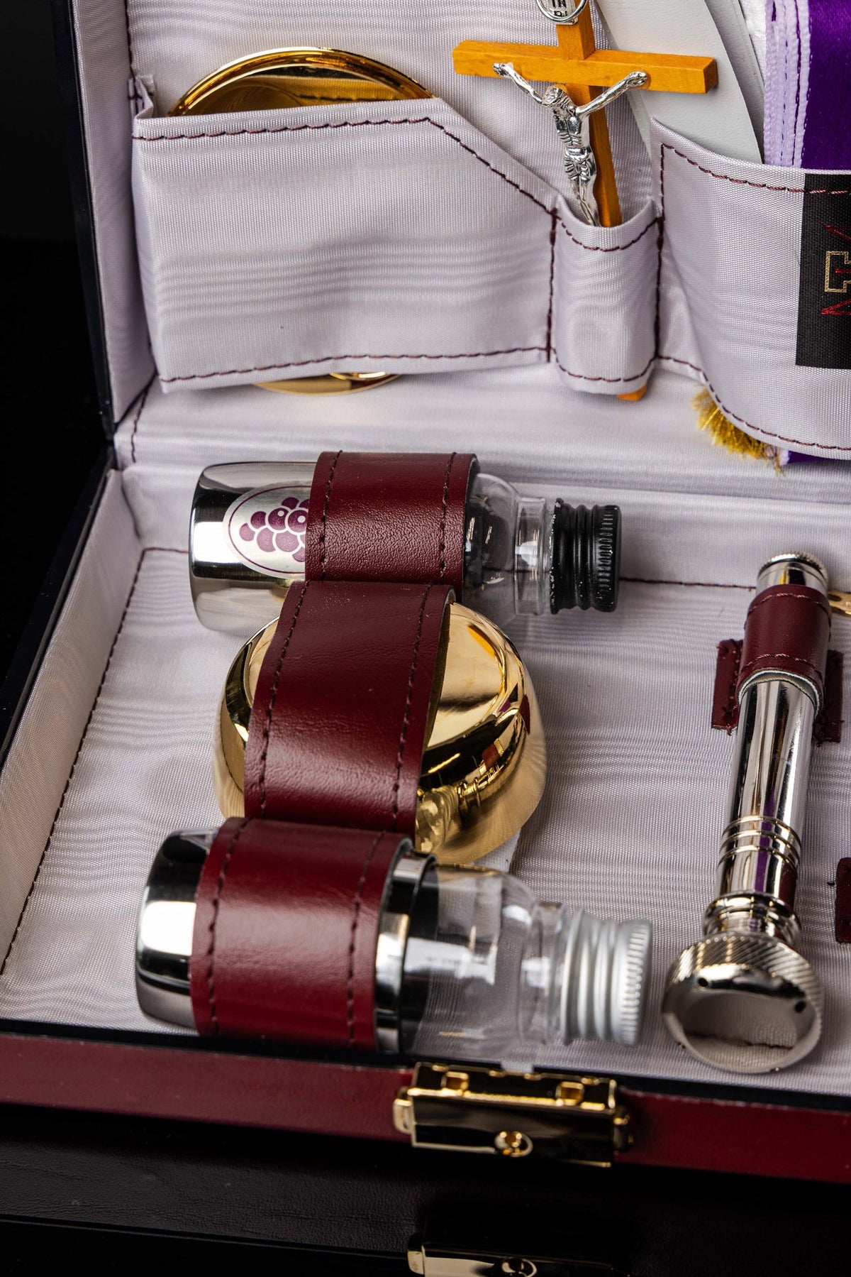 Close-up of liturgical suitcase with gold vessel, crucifix and strapped glass bottles