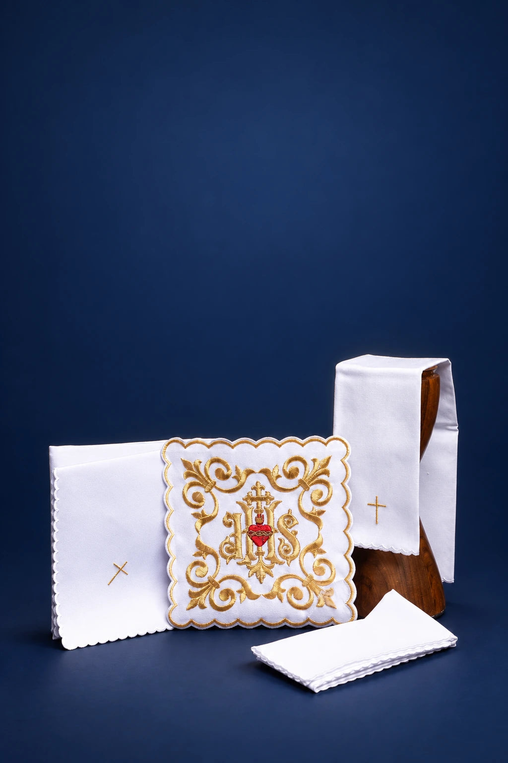 Embroidered altar linen set with central IHS motif, scalloped cloth, folded purificator, and cross detail