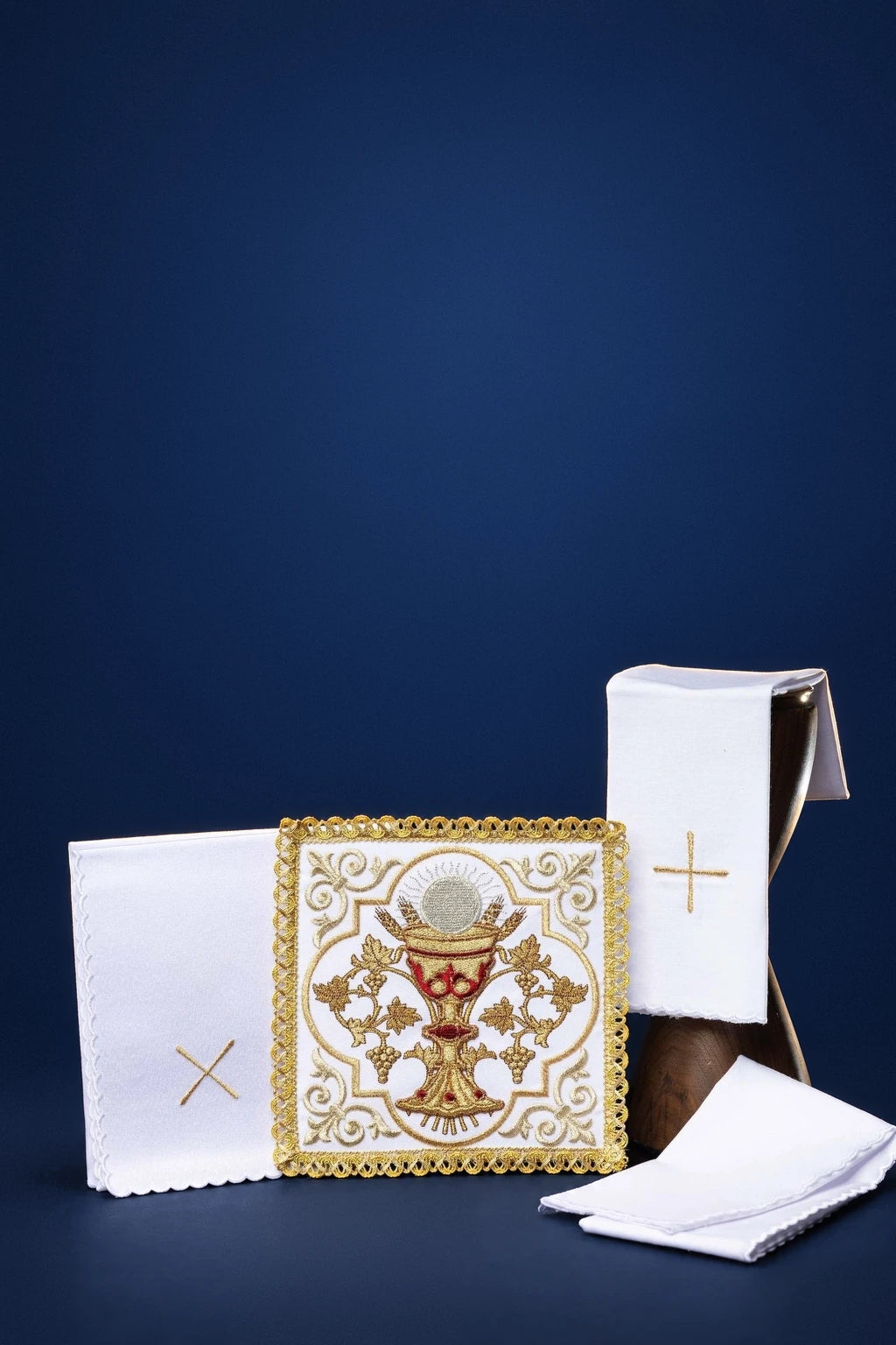 Embroidered altar linen set with chalice motif and gold cross, shown with folded cloths and a purificator