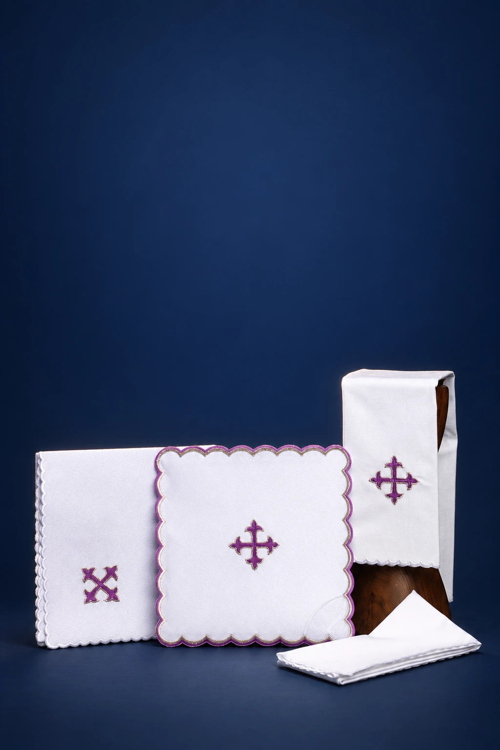 Embroidered altar linen set with purple cross motifs and scalloped edges, shown folded and stacked