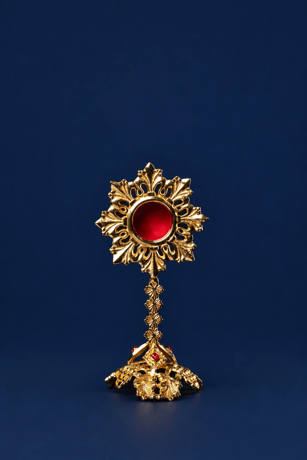 Front view of brass reliquary with sunburst top and red center on ornate base