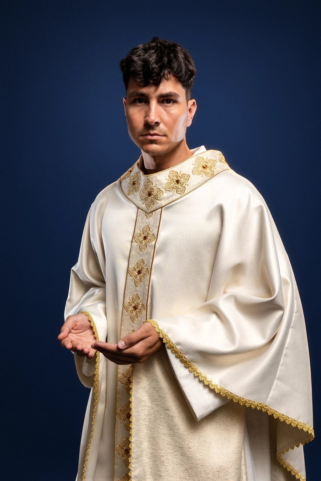 Front view of an ecru chasuble with embroidered gold orphrey and stone-trimmed collar and hem border