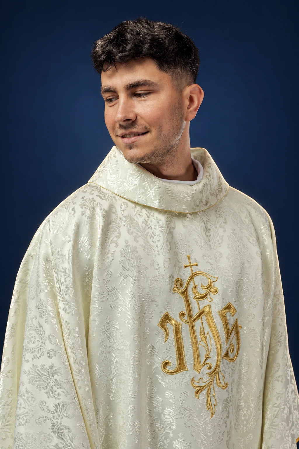 Front view of an ecru chasuble with a gold embroidered IHS motif and subtle jacquard pattern