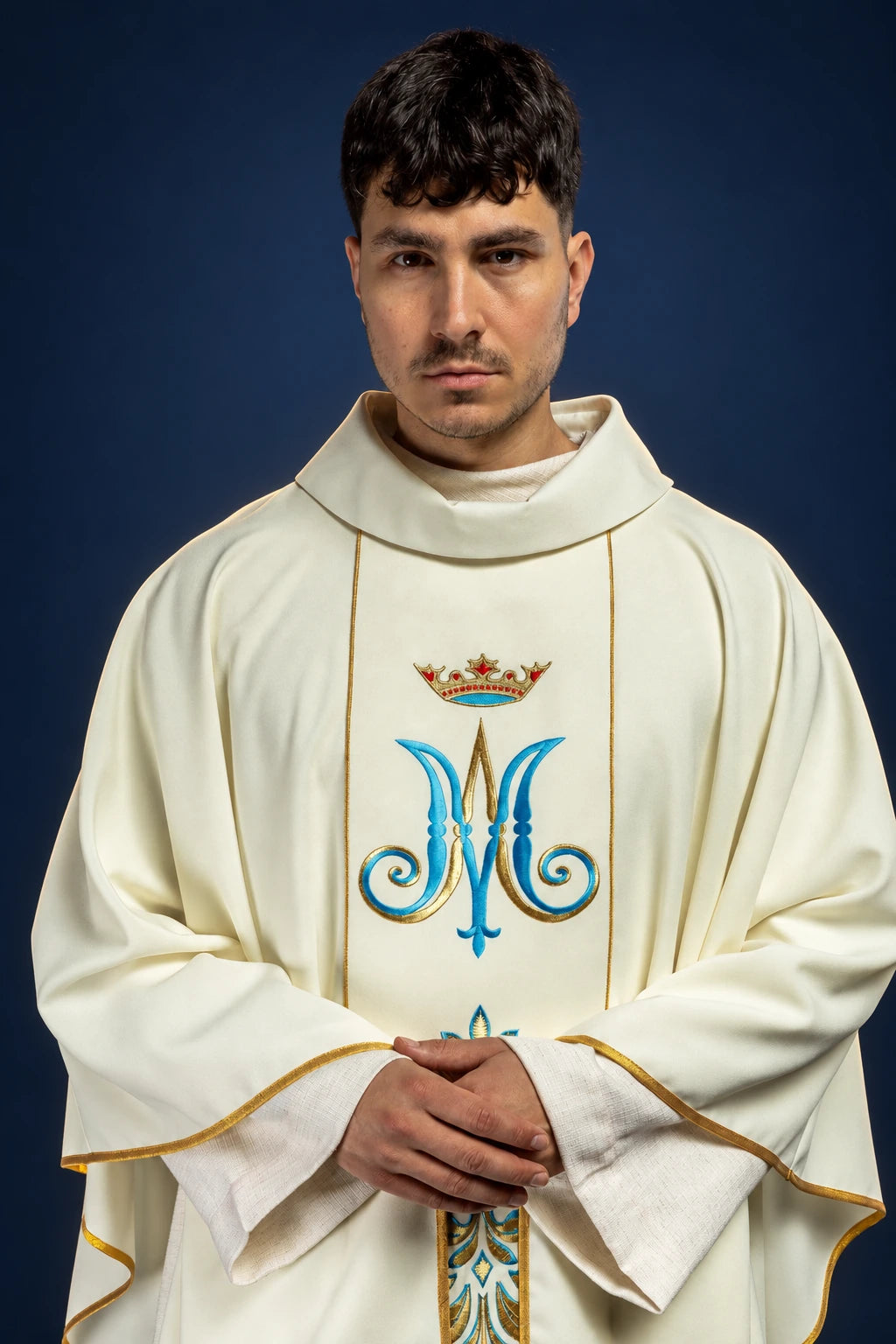 Front view of an ecru chasuble with hooded collar and ornate Marian monogram on the chest panel