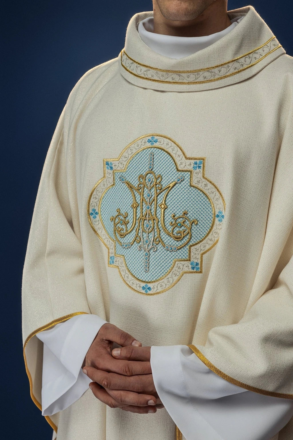 Front view of an ecru chasuble with a Marian embroidered motif and gold trim at the collar and sleeves
