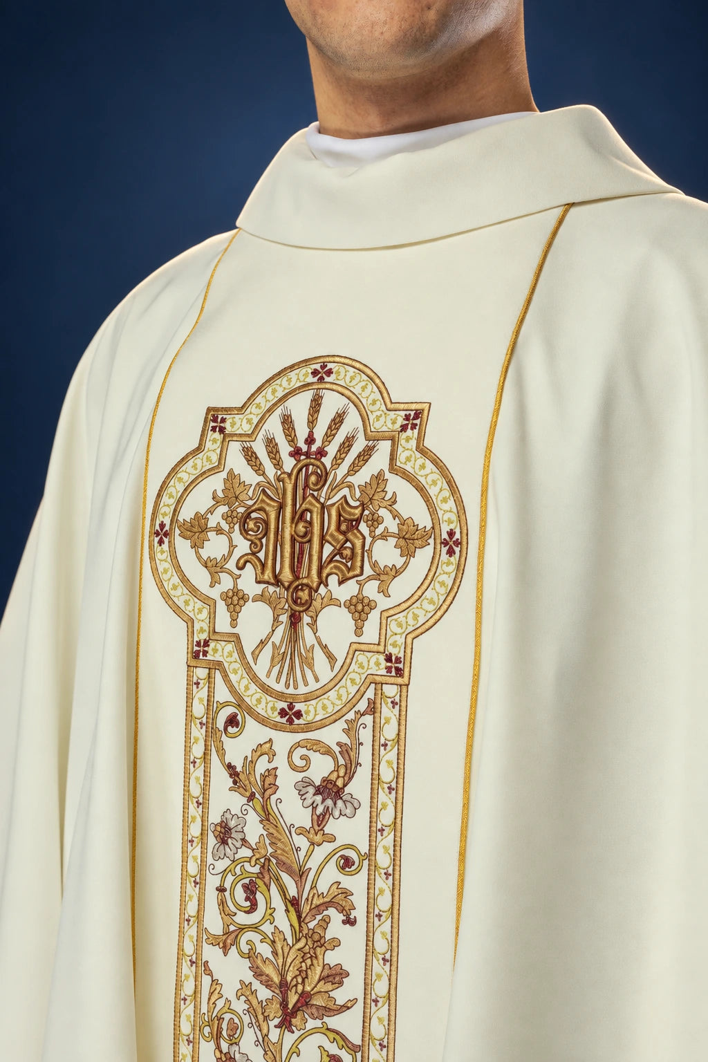 Front view of an ecru chasuble with ornate gold trim and central IHS embroidery panel