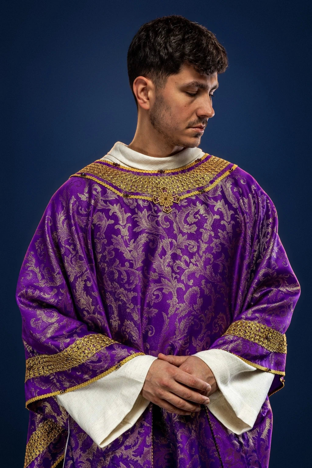 Front view of a purple chasuble with gold trim and ornate floral pattern over a white alb collar and sleeves