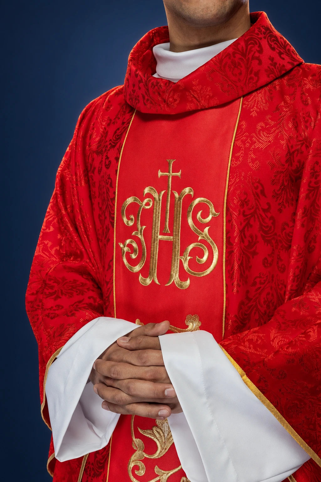 Front view of a red chasuble with gold IHS embroidery on the orphrey and matching ornate patterned fabric