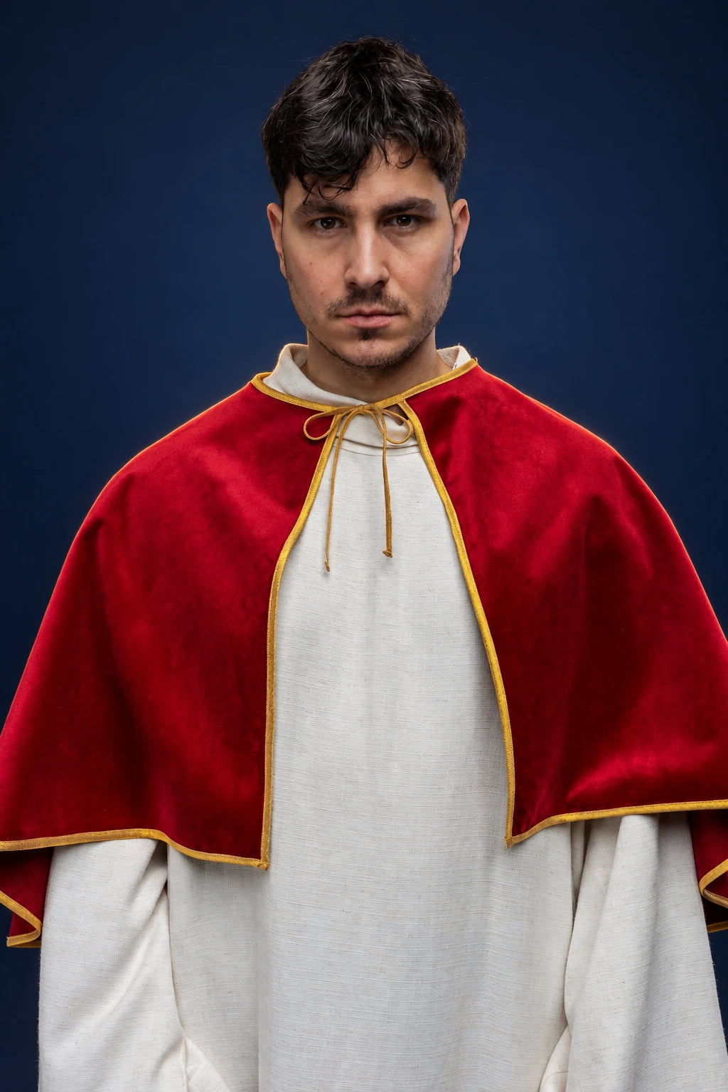 Front view of a red velvet altar server cape with gold trim and tie closure, worn over a white robe