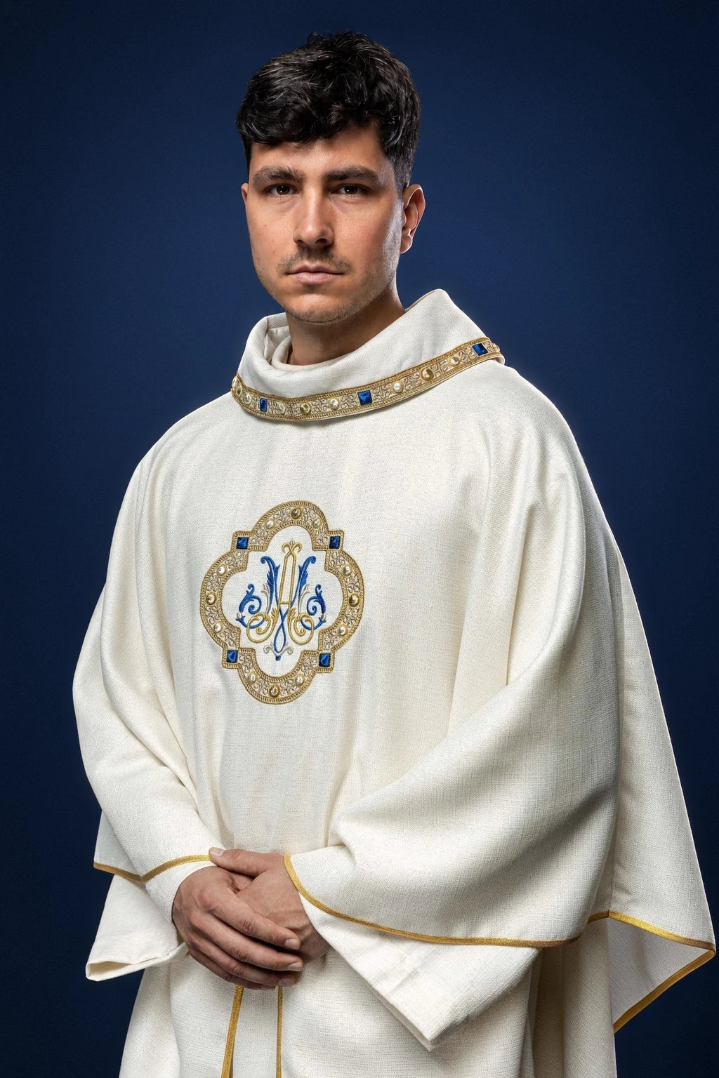 Front view of a white chasuble with gold trim and an embroidered Marian emblem on the chest