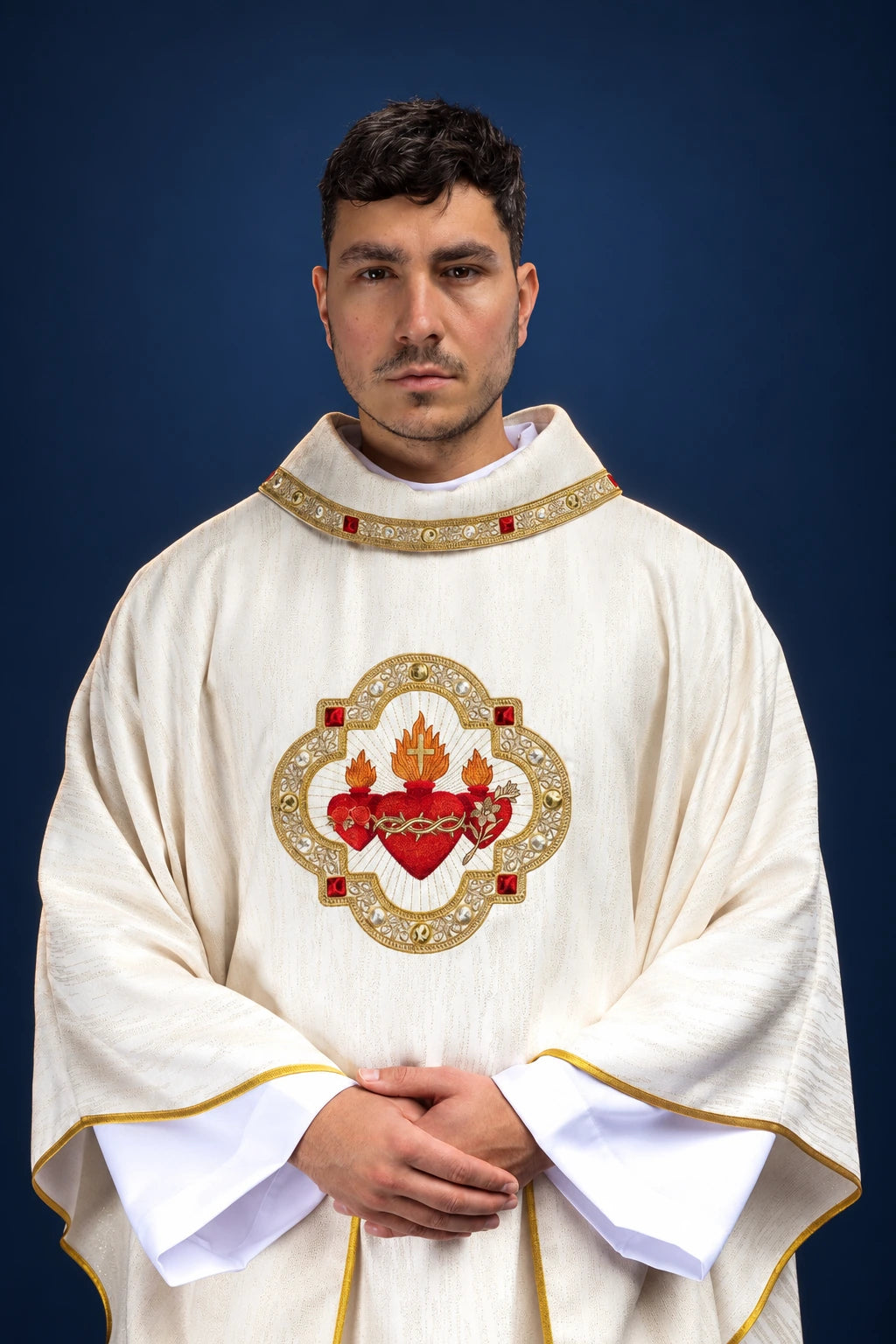 Front view of a white chasuble with gold trim and embroidered Sacred Hearts medallion on the chest