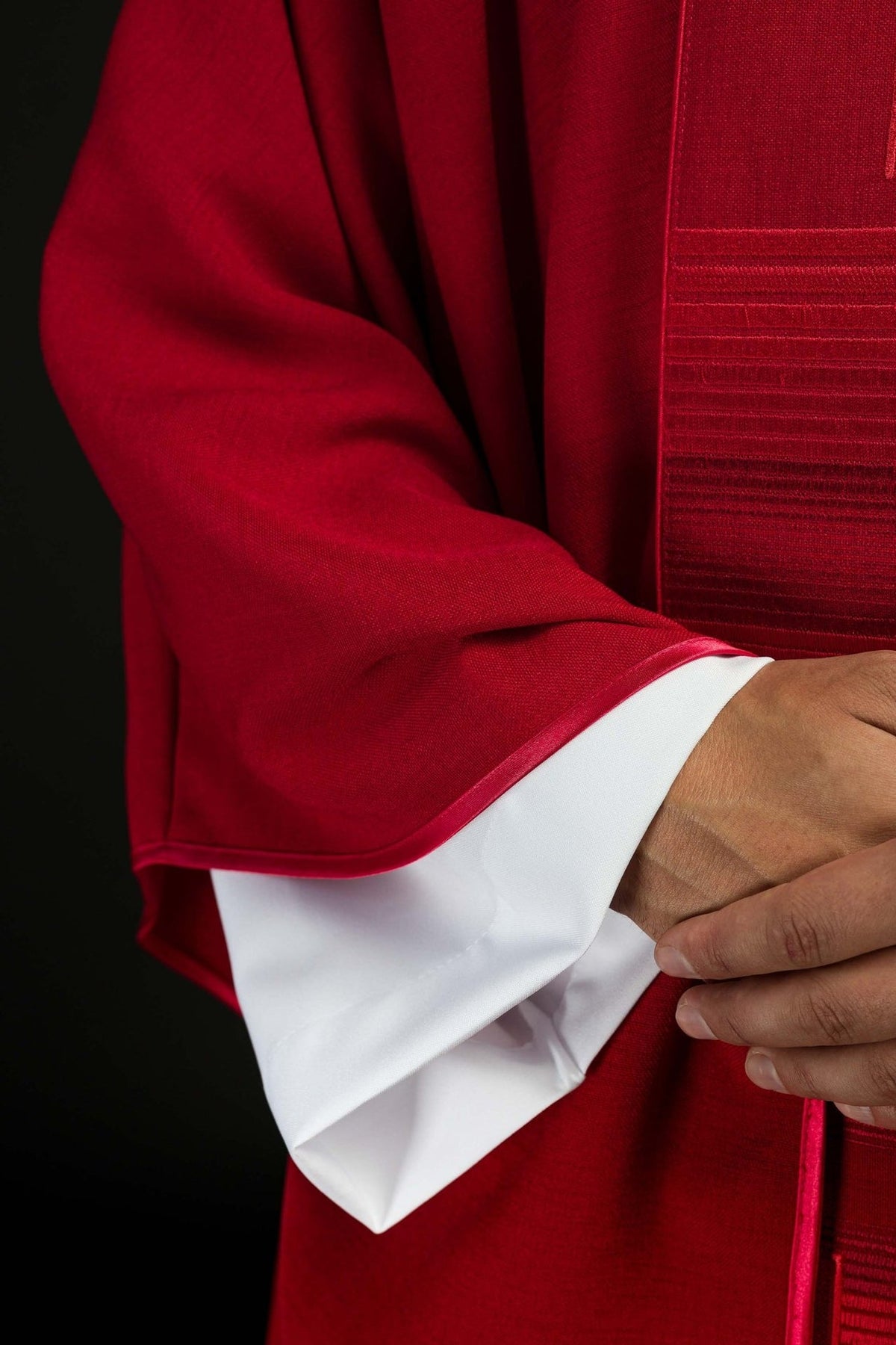 Red chasuble sleeve close-up with red trim and white cuff visible