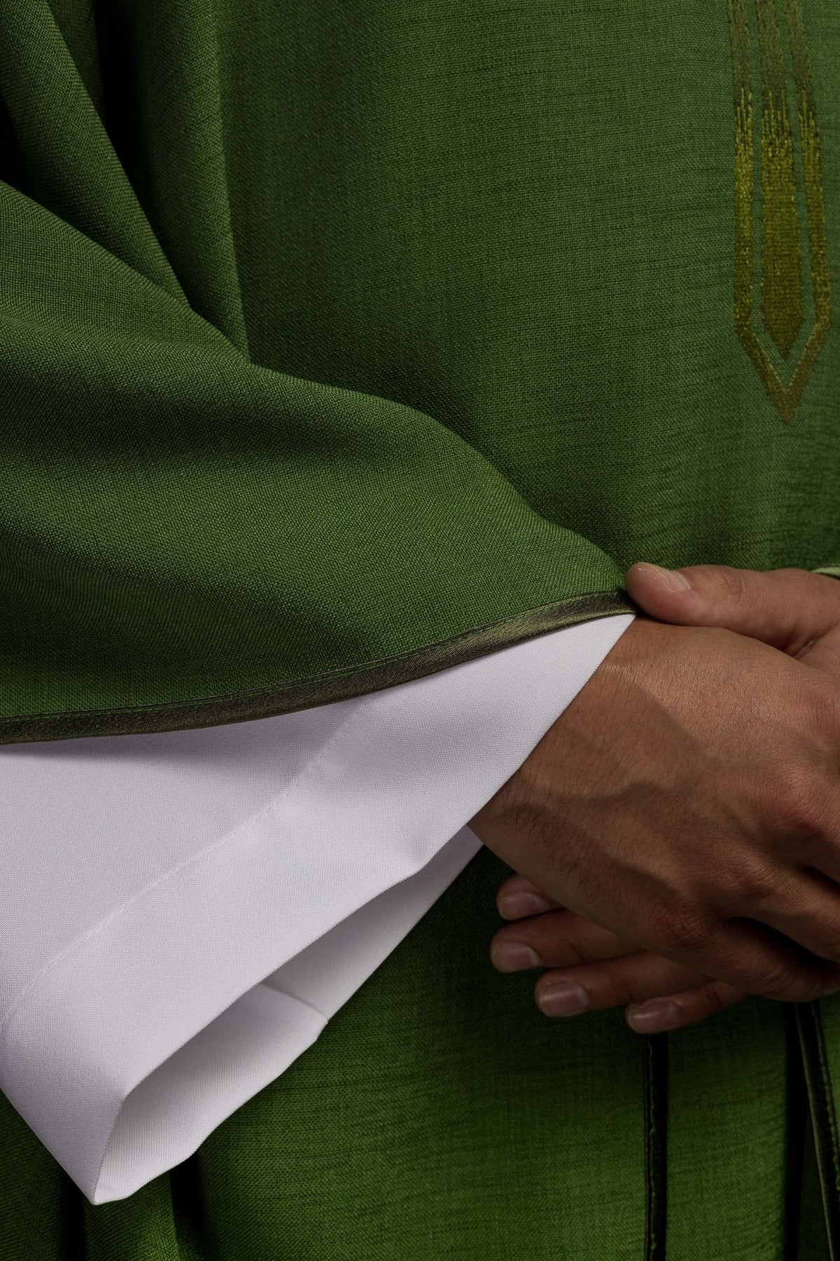 Green chasuble detail showing woven fabric, embroidered cross and dark trim
