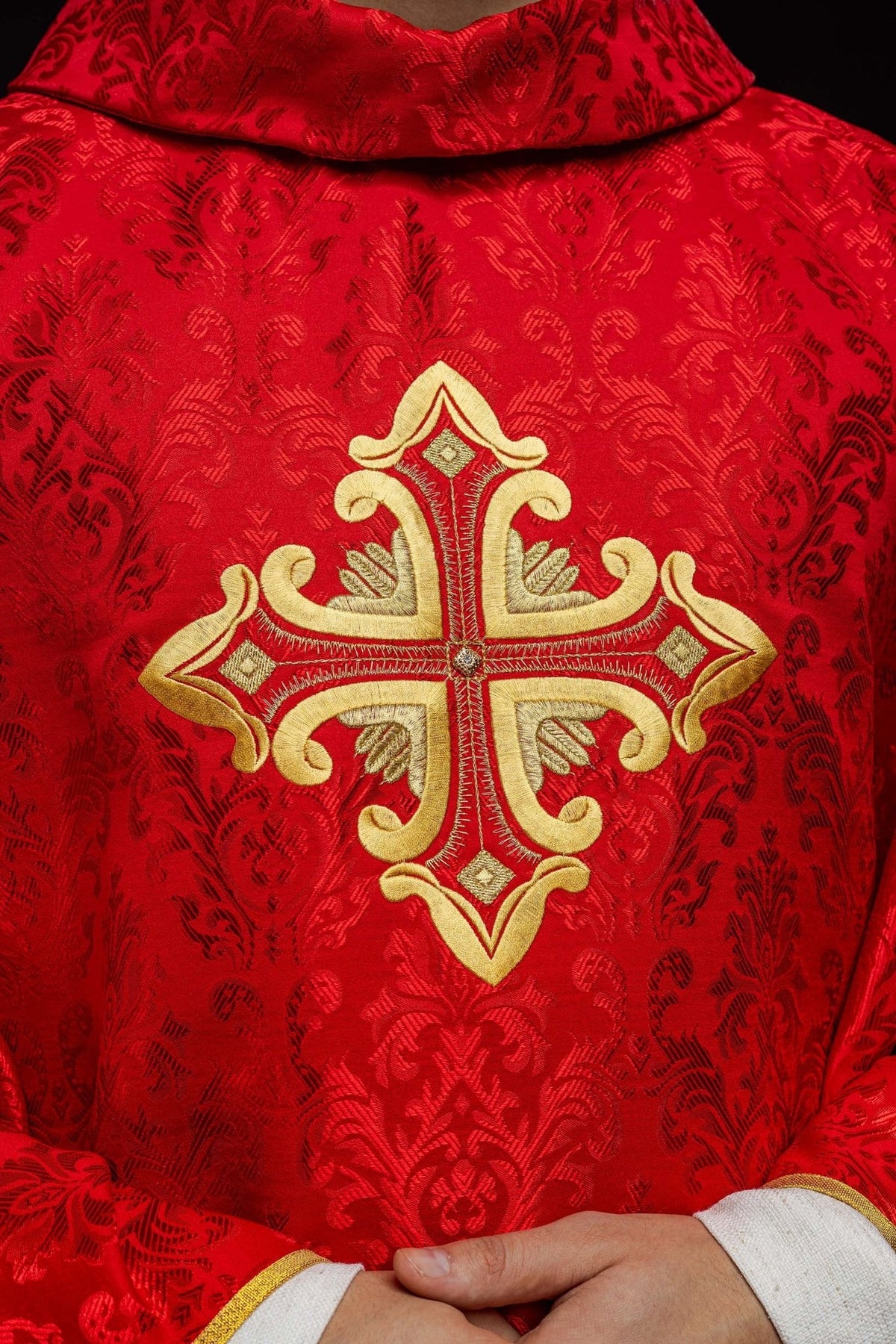 Red chasuble close-up with gold embroidered cross on patterned fabric