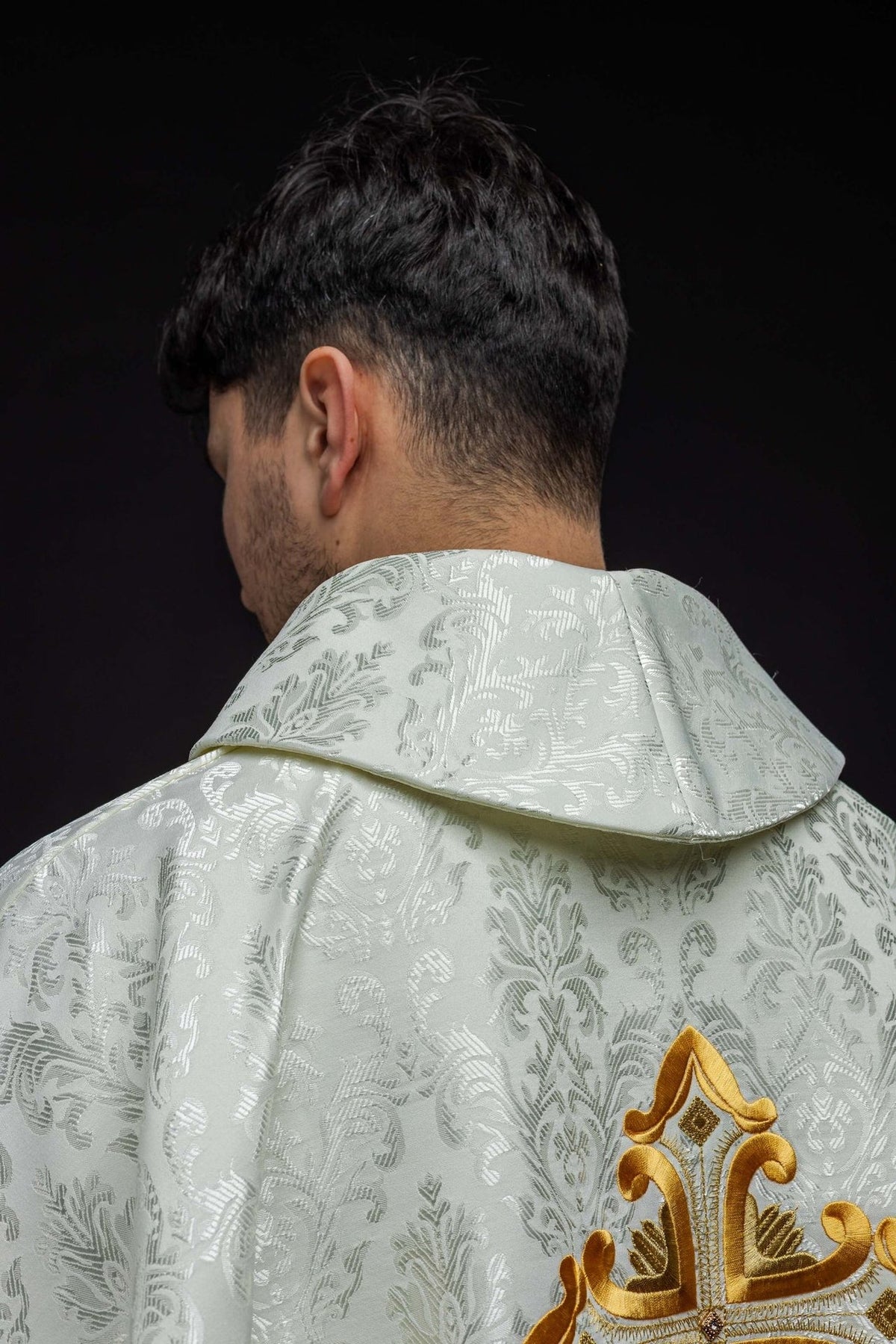 Ecru chasuble back view with patterned fabric and partial gold cross embroidery